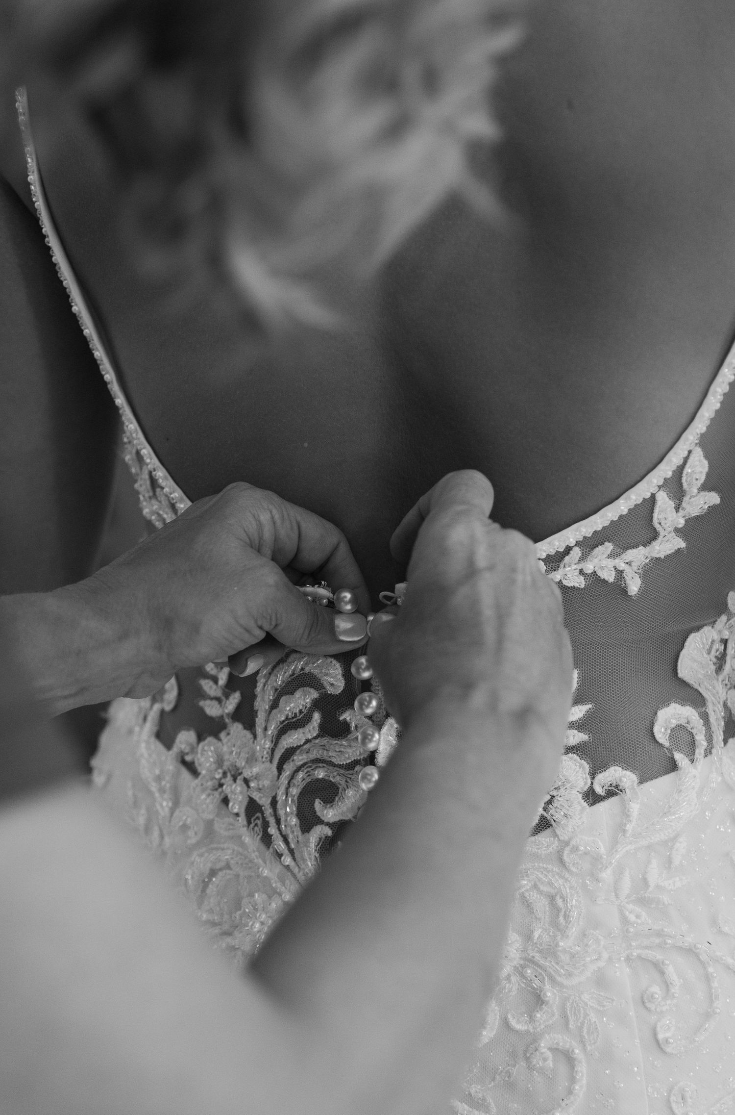 A close-up black and white detail shot of delicate lace embroidery on wedding dress fabric.