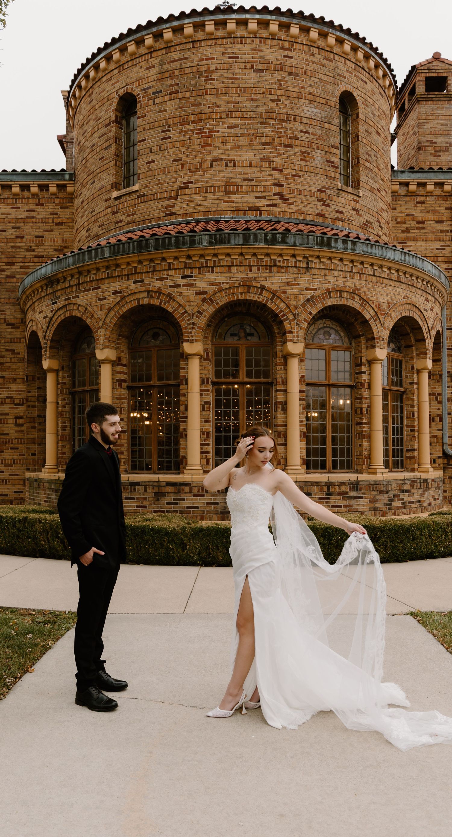 A wedding couple poses outside Nazareth Hall with arched windows and Romanesque architecture.