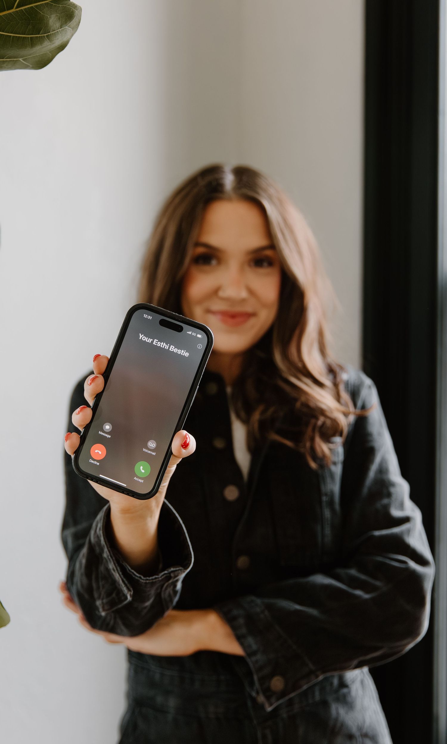 Woman in black jacket holding smartphone showing incoming call screen toward camera.