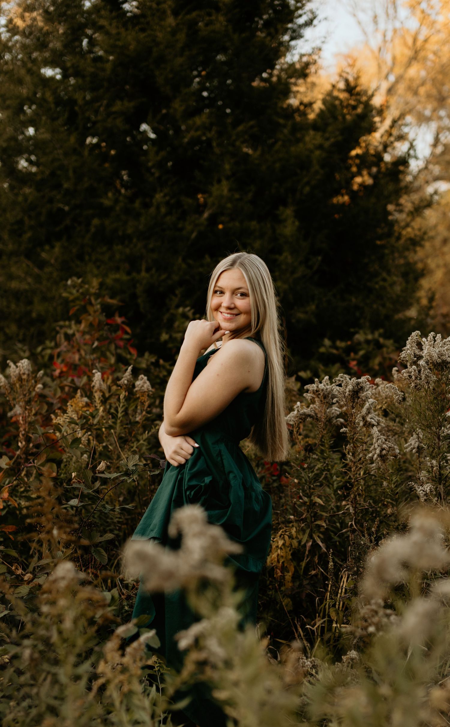 Outdoor portrait in emerald dress surrounded by autumn wildflowers at sunset.