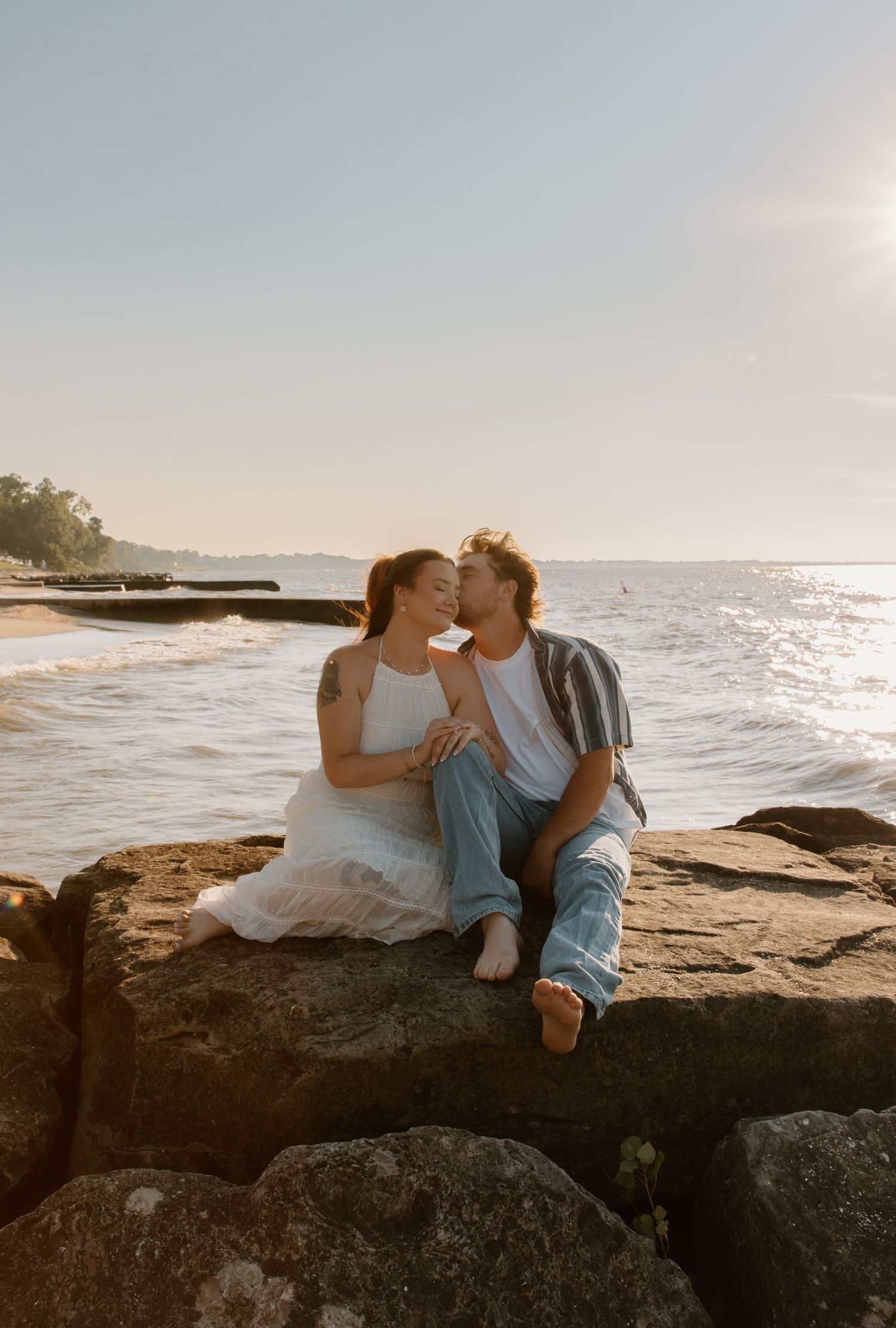 Couple sitting on rocky beach sharing a romantic moment at golden hour with ocean waves in background.