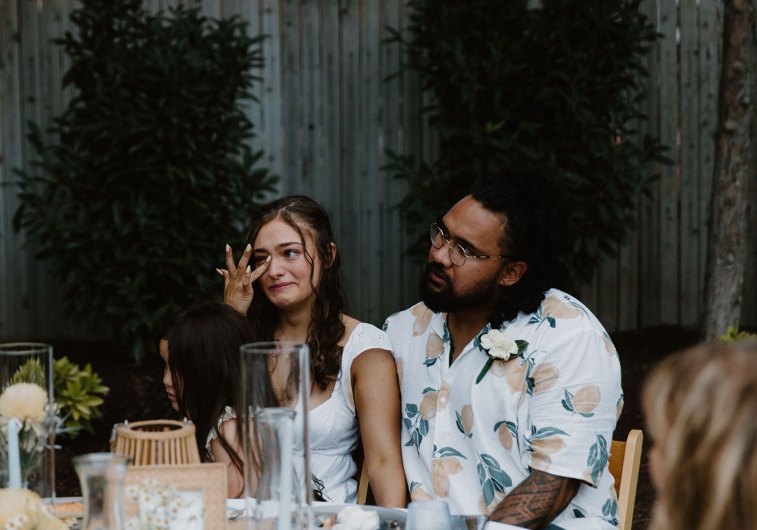 Wedding guests enjoy an outdoor reception dinner at long tables decorated with white linens and floral centerpieces.