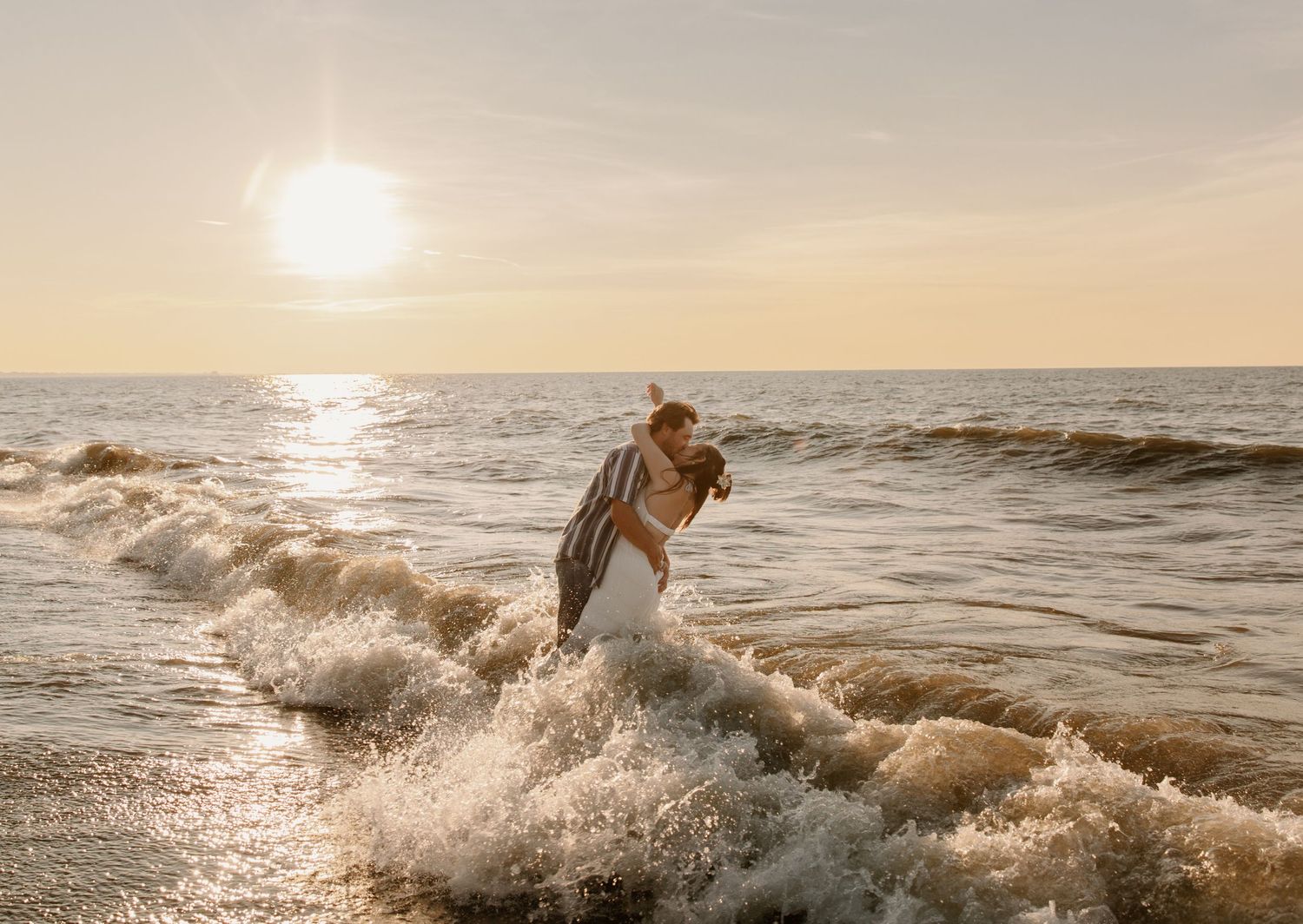 Couple sharing a romantic kiss in ocean waves at golden sunset on a beautiful beach.