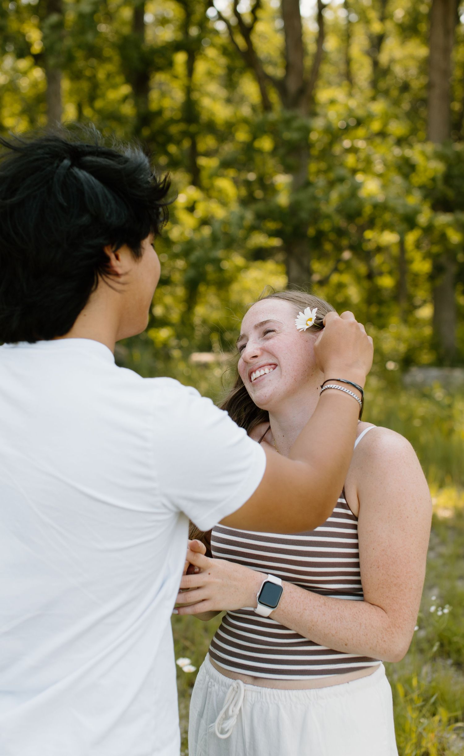 Joyful couple laughs and embraces while wearing black and white stripes and standing in a sunlit wooded area.