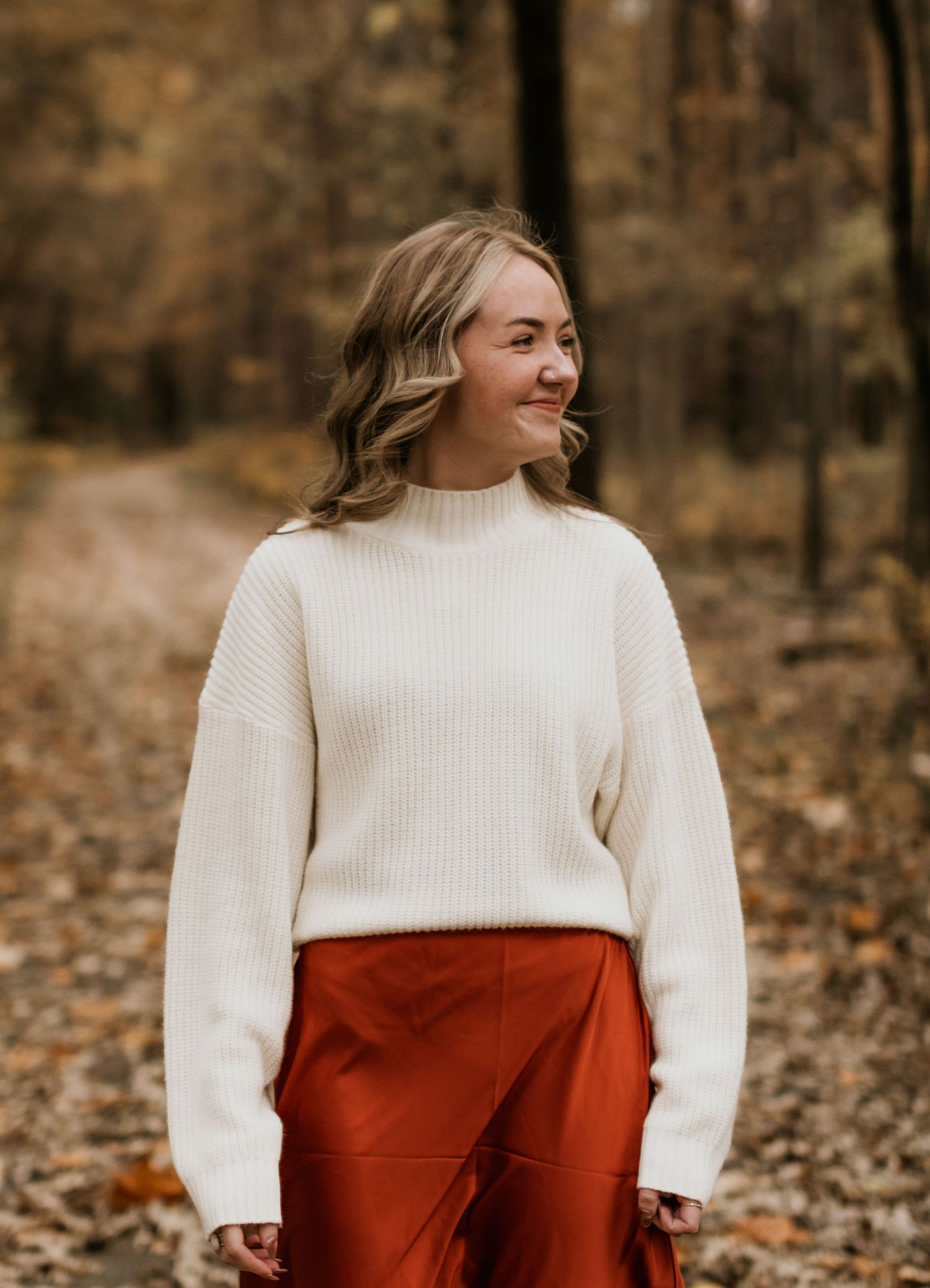 Autumn portrait featuring cream sweater and rust-colored skirt against fall foliage.