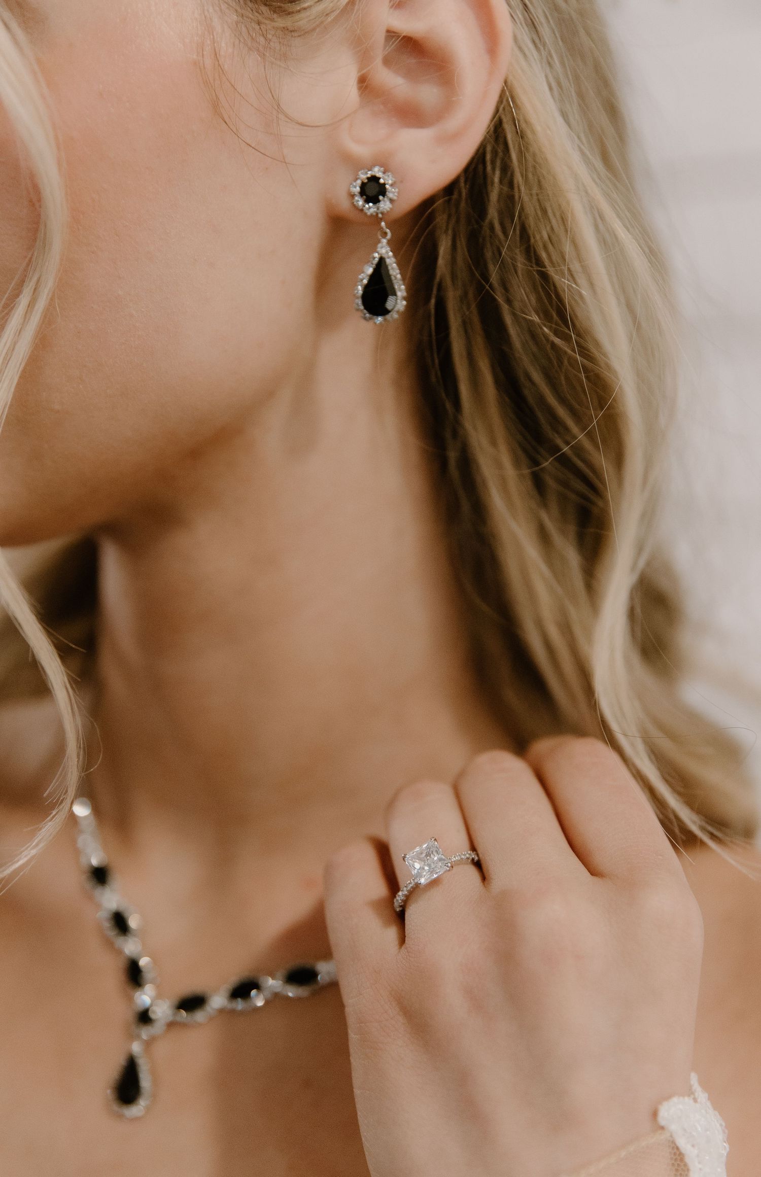 Woman wearing black and silver crystal drop earrings, matching necklace, and a diamond engagement ring.