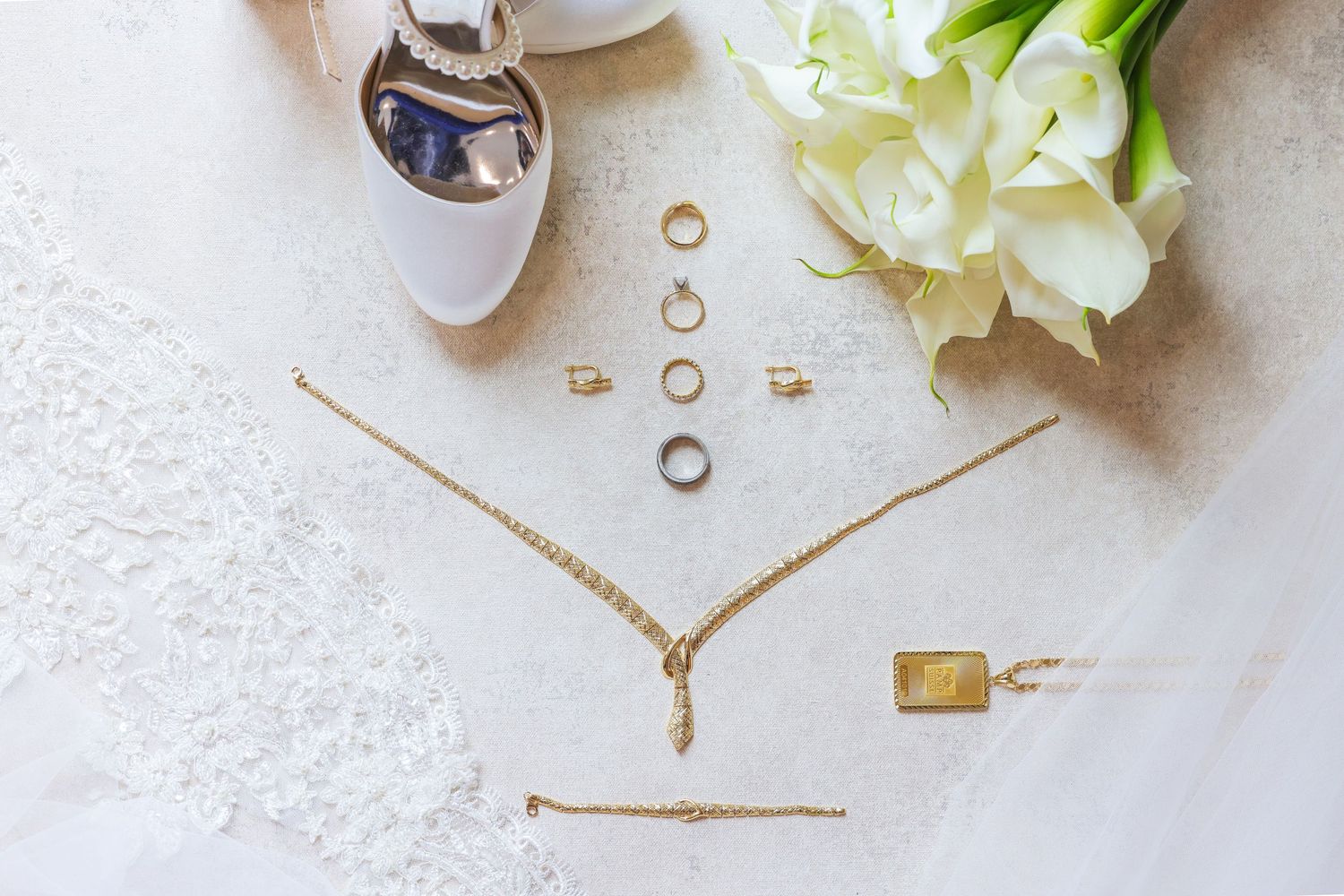 Elegant bridal jewelry and white tulips arranged on light fabric with wedding rings.