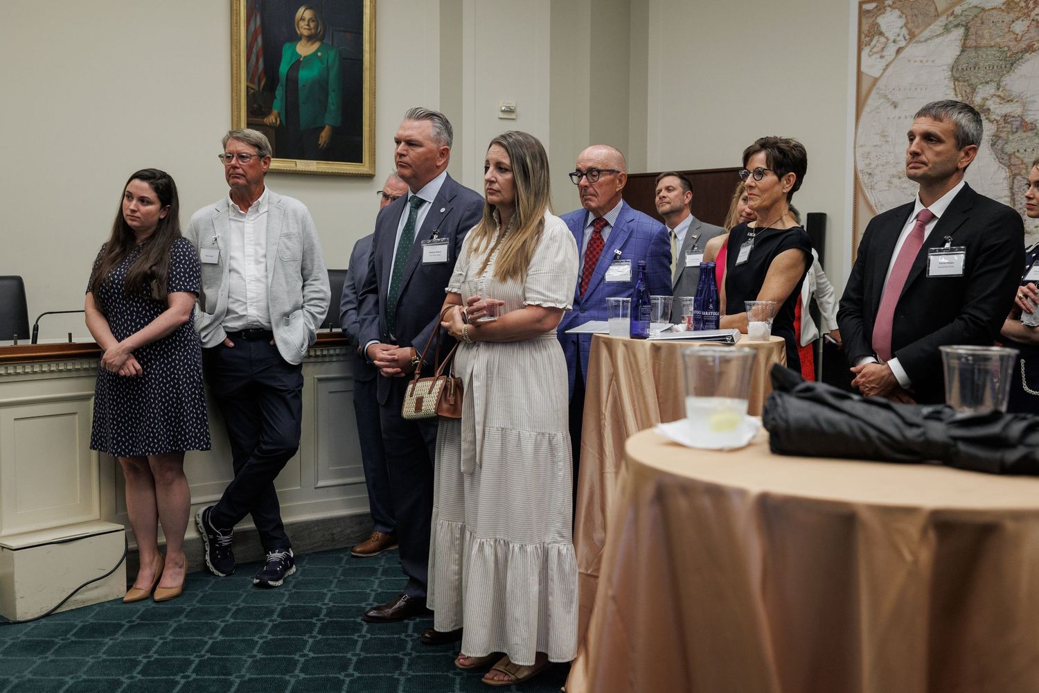 Group of professionals standing attentively in a formal meeting room with portrait painting and world map on wall.