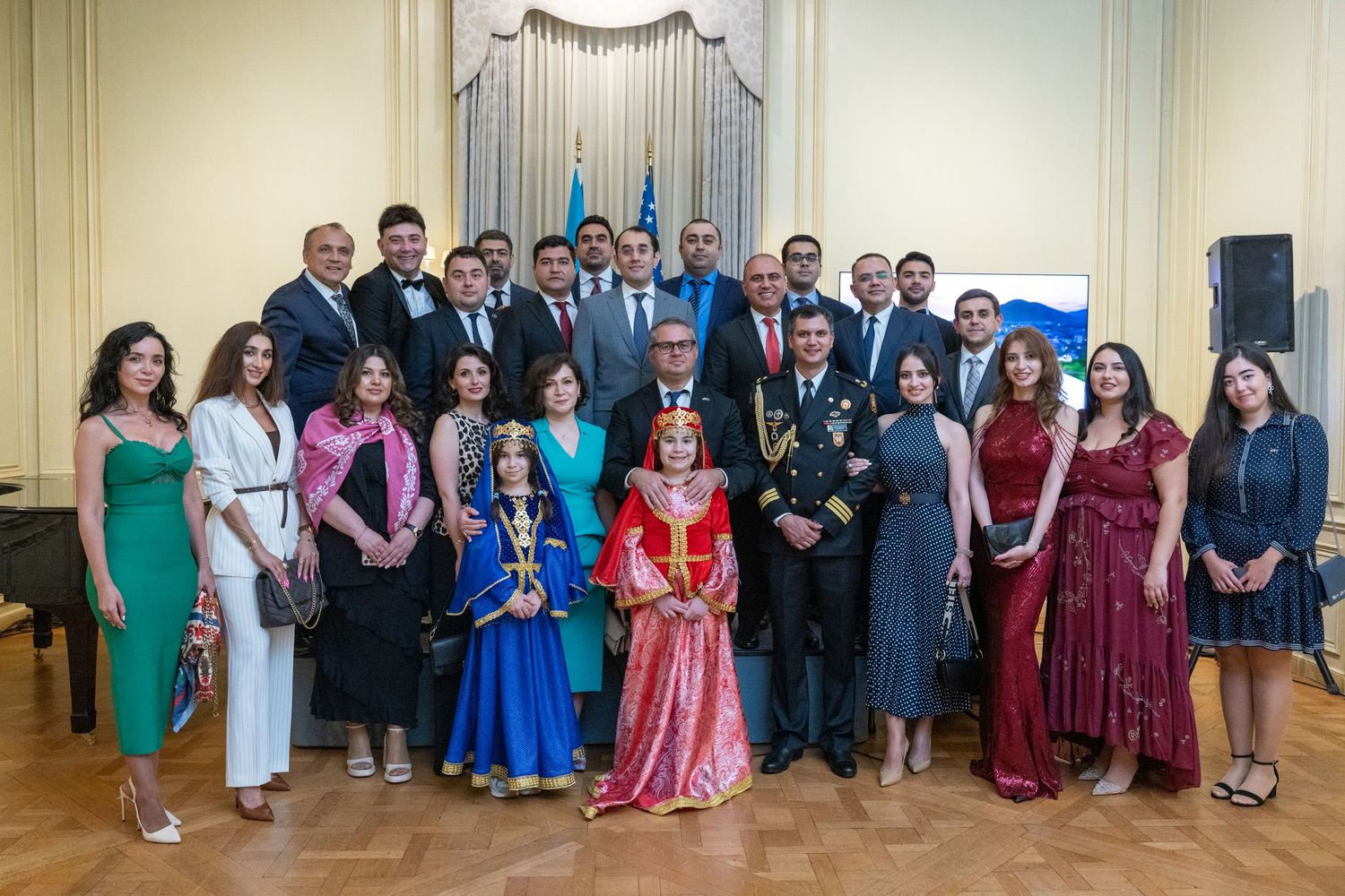 A panoramic view of a formal event with guests in elegant attire standing in a grand room with white walls and columns.