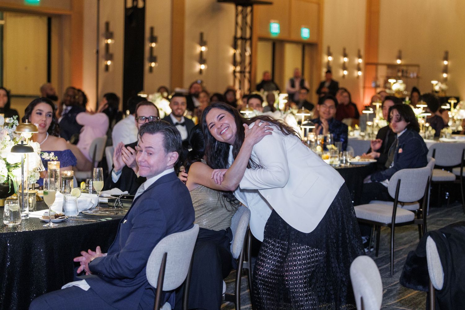 A crowded banquet hall with people seated at round tables during a formal event.