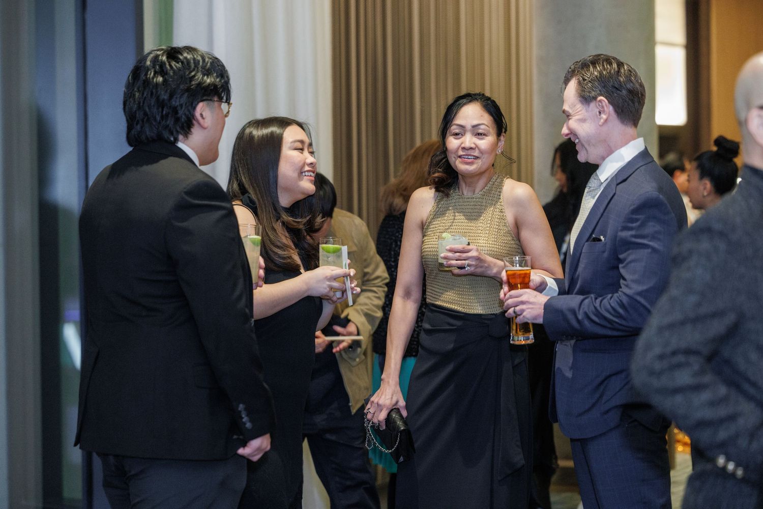 Elegantly dressed guests socializing at an upscale cocktail reception, holding drinks in a modern venue.