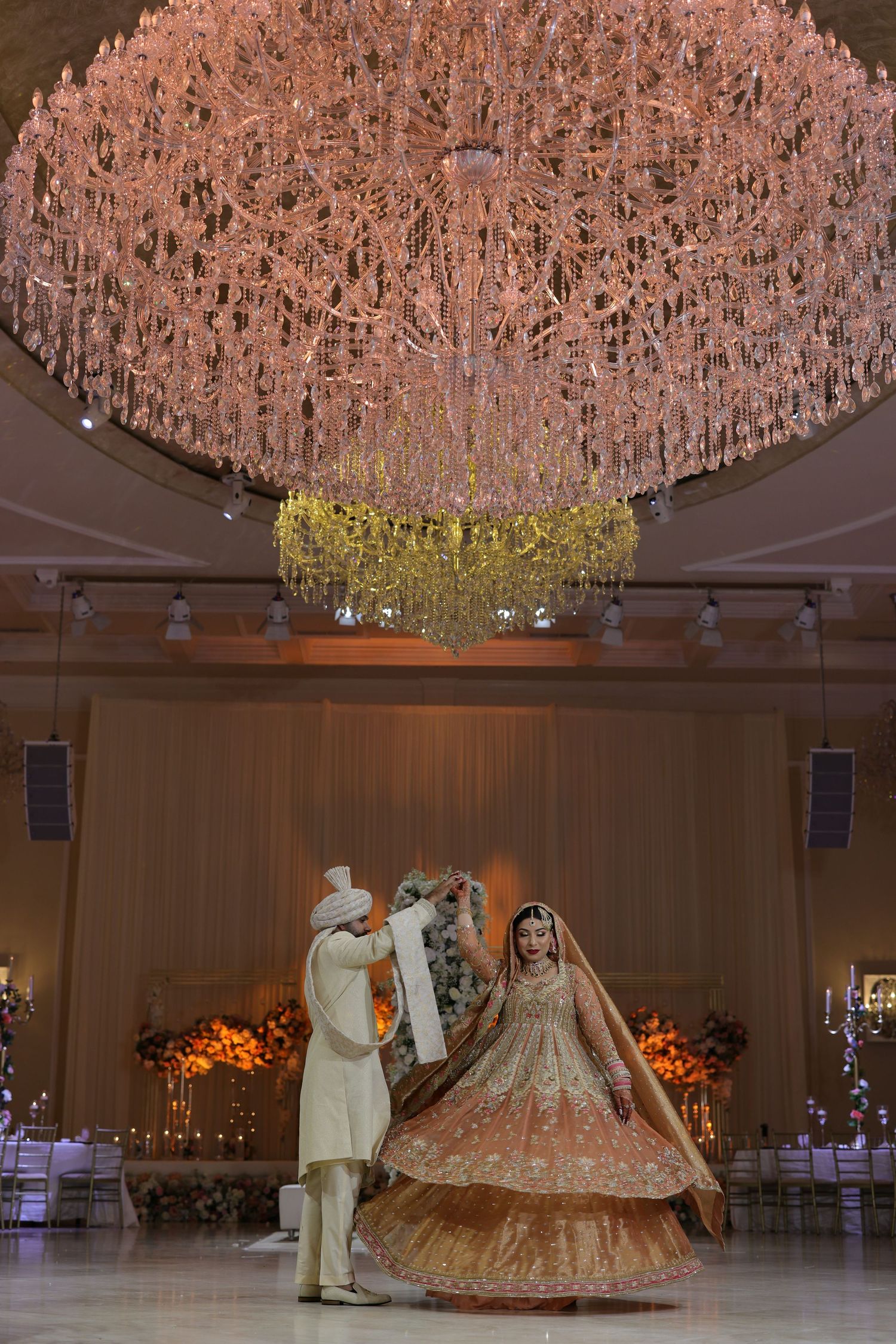 Elegant wedding ceremony under a stunning pink crystal chandelier with ornate decor in a luxurious ballroom.