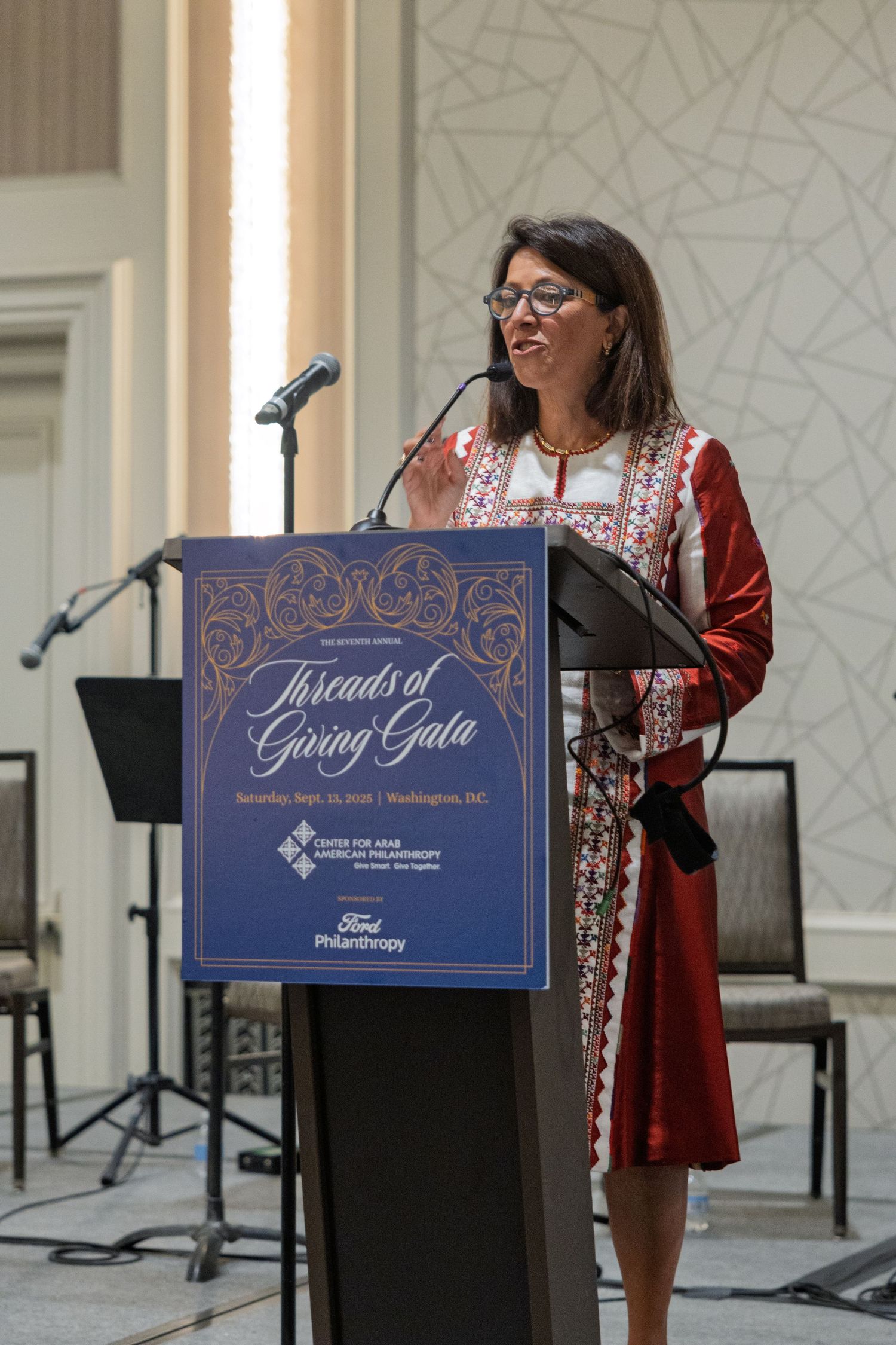 Speakers at a podium with blue decorative signage during a formal event presentation.