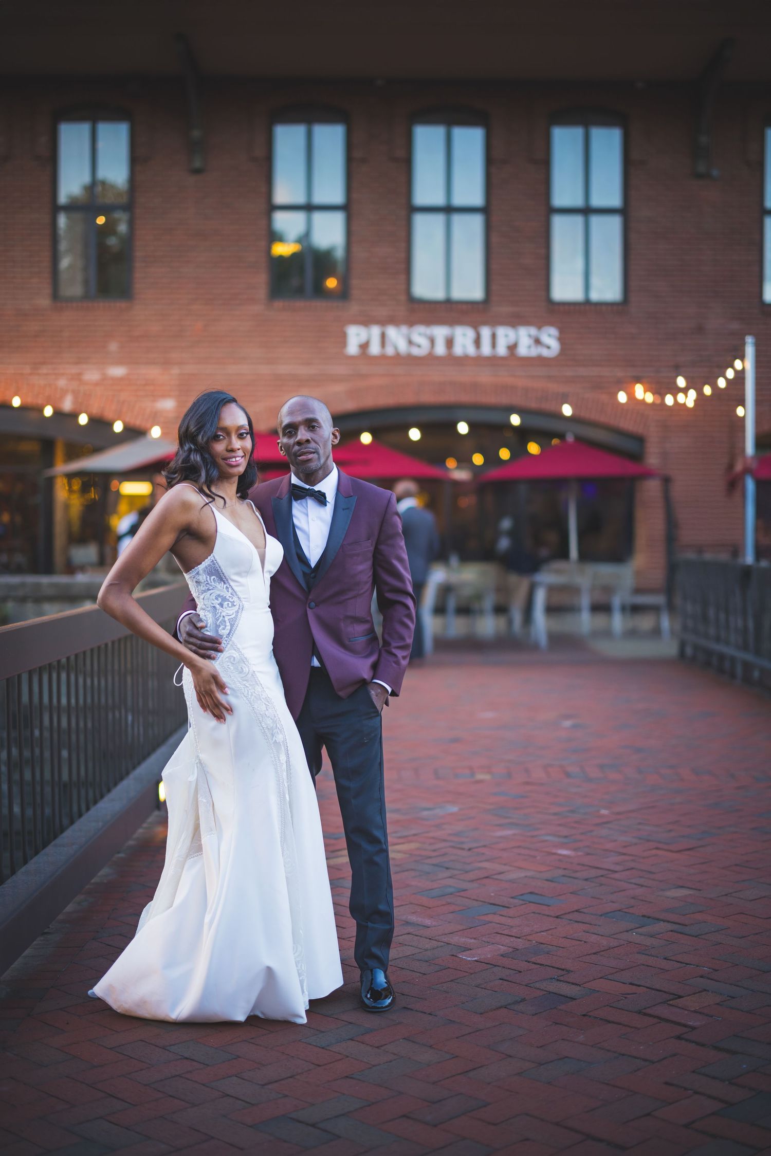 Two people dancing together on a brick patio at dusk with festive string lights visible in the background.