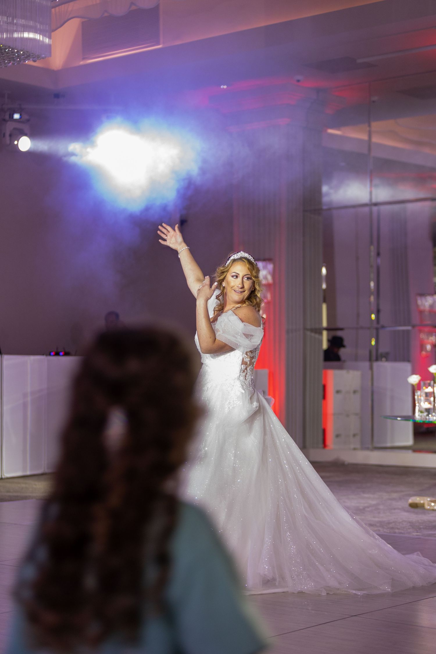 A person in a flowing white wedding gown dances gracefully under dramatic purple and blue lighting in an event space.
