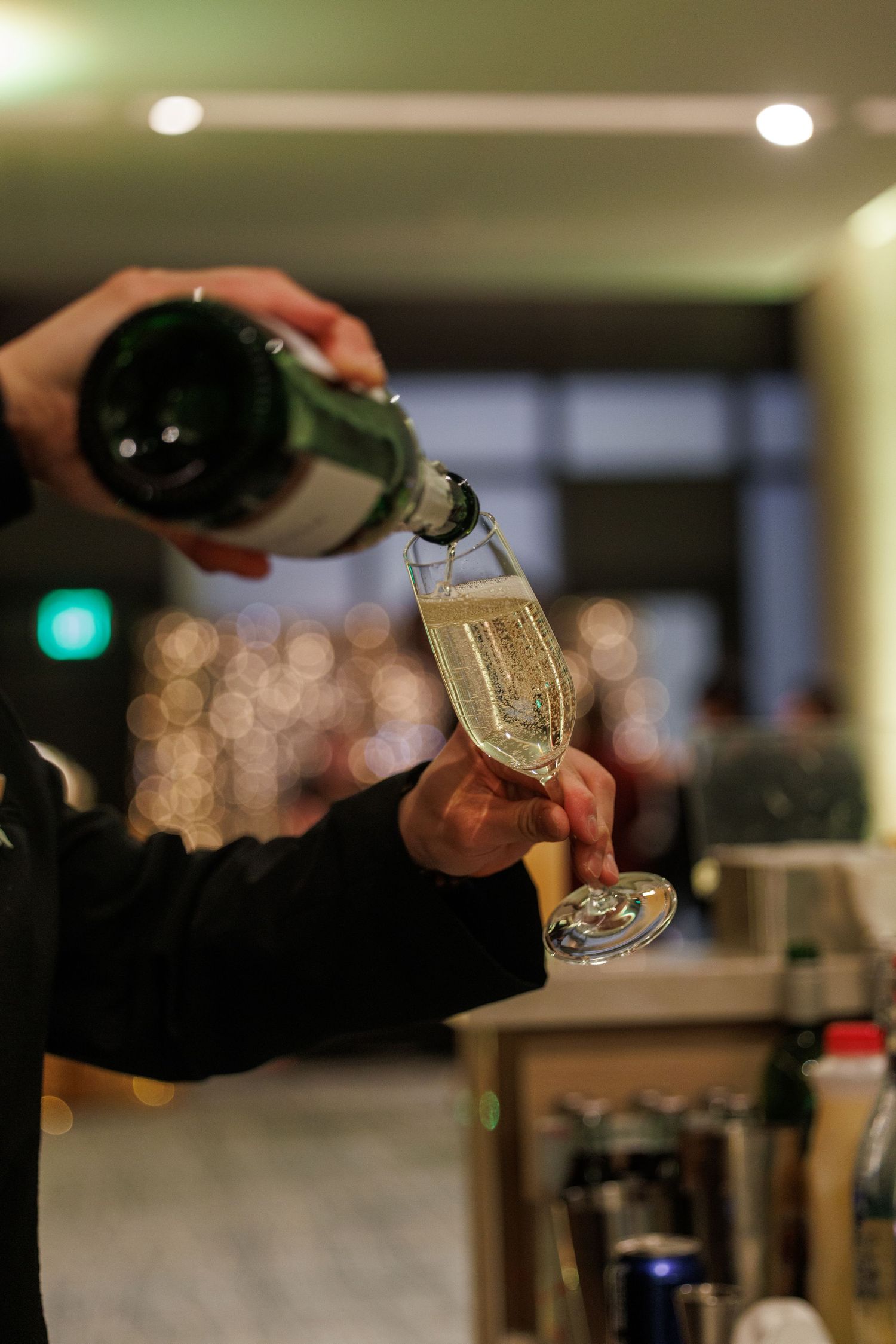 Hands pour a golden liquid into a glass with precise control in a dimly lit bar setting.