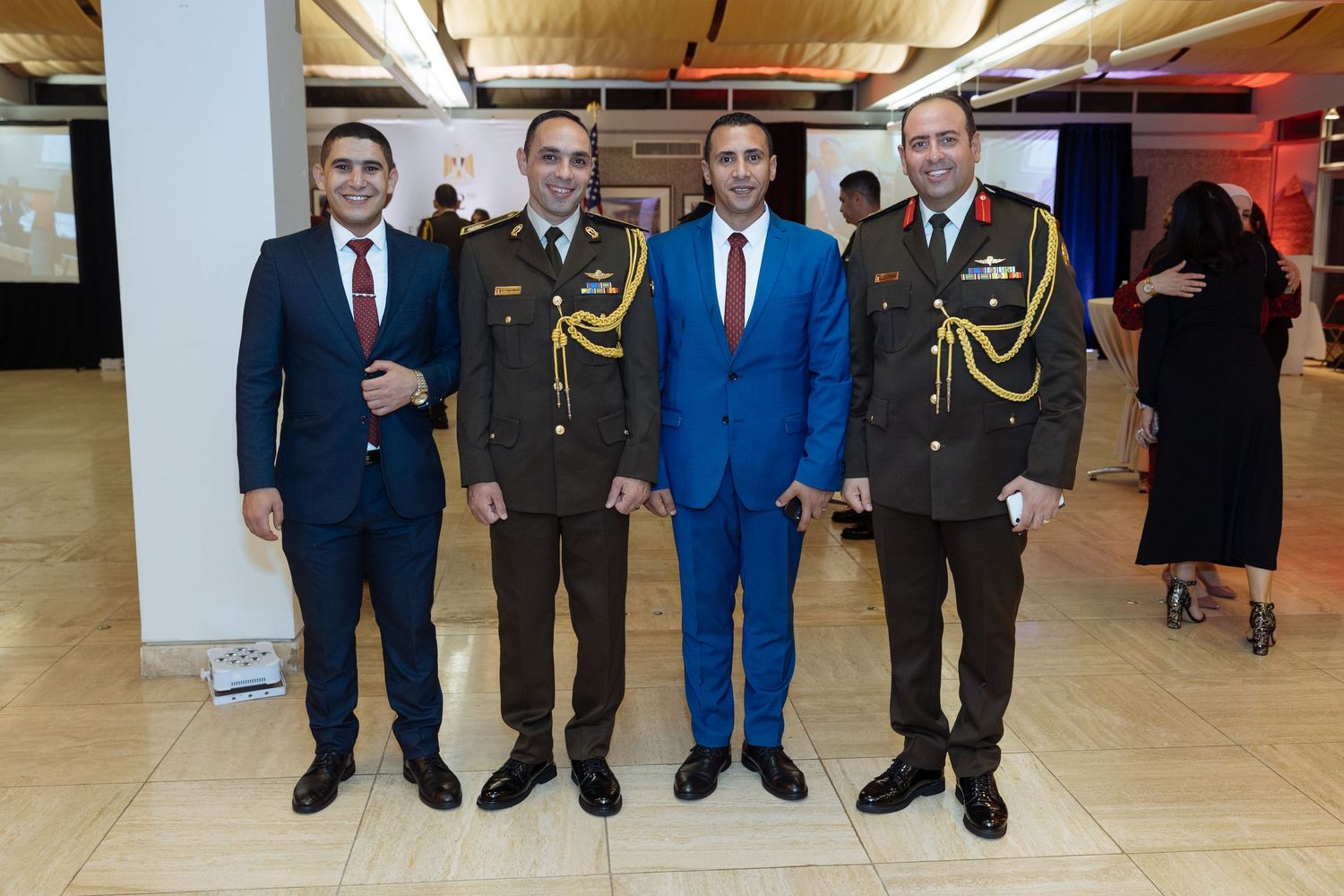 Group of people in formal business attire standing in a line against a beige wall.
