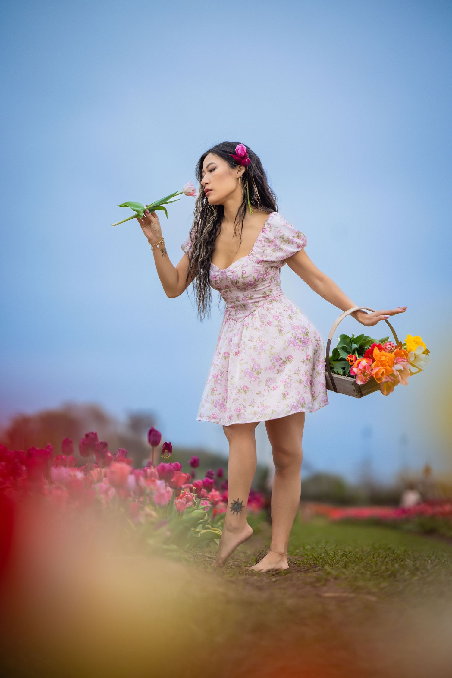 Woman in pink floral dress dancing with flowers in garden against blue sky.