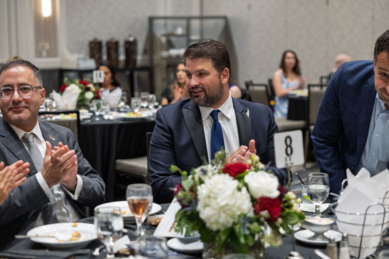 Wedding guests enjoy dinner and conversation at an elegant reception table decorated with floral centerpieces.