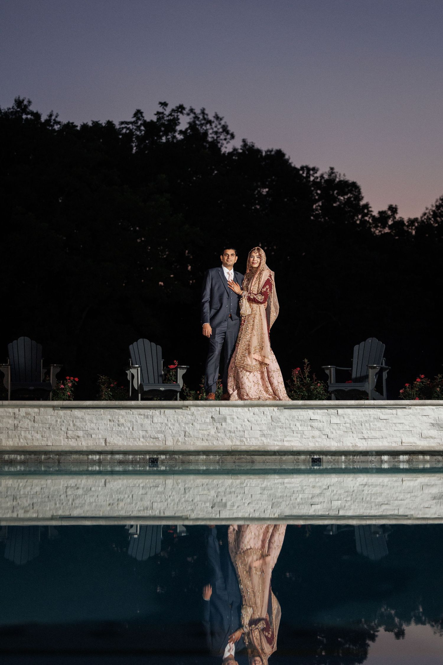 A couple stands by a pool at dusk, creating a romantic silhouette against the evening sky.
