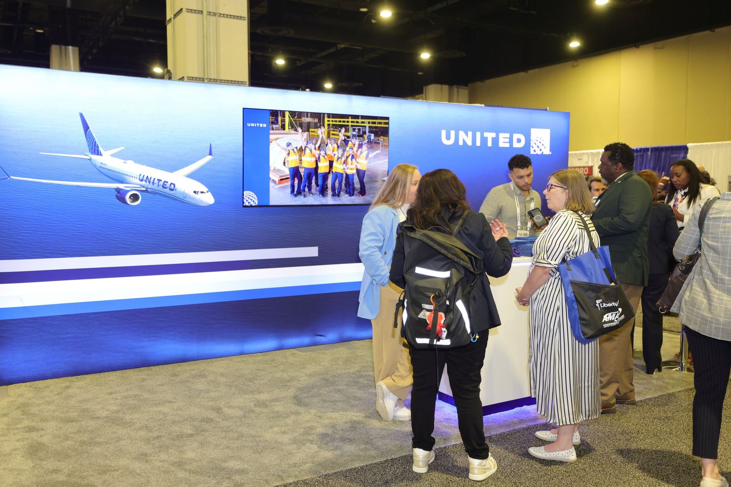 People gather at a United Airlines trade show booth featuring a plane graphic and blue branding display.