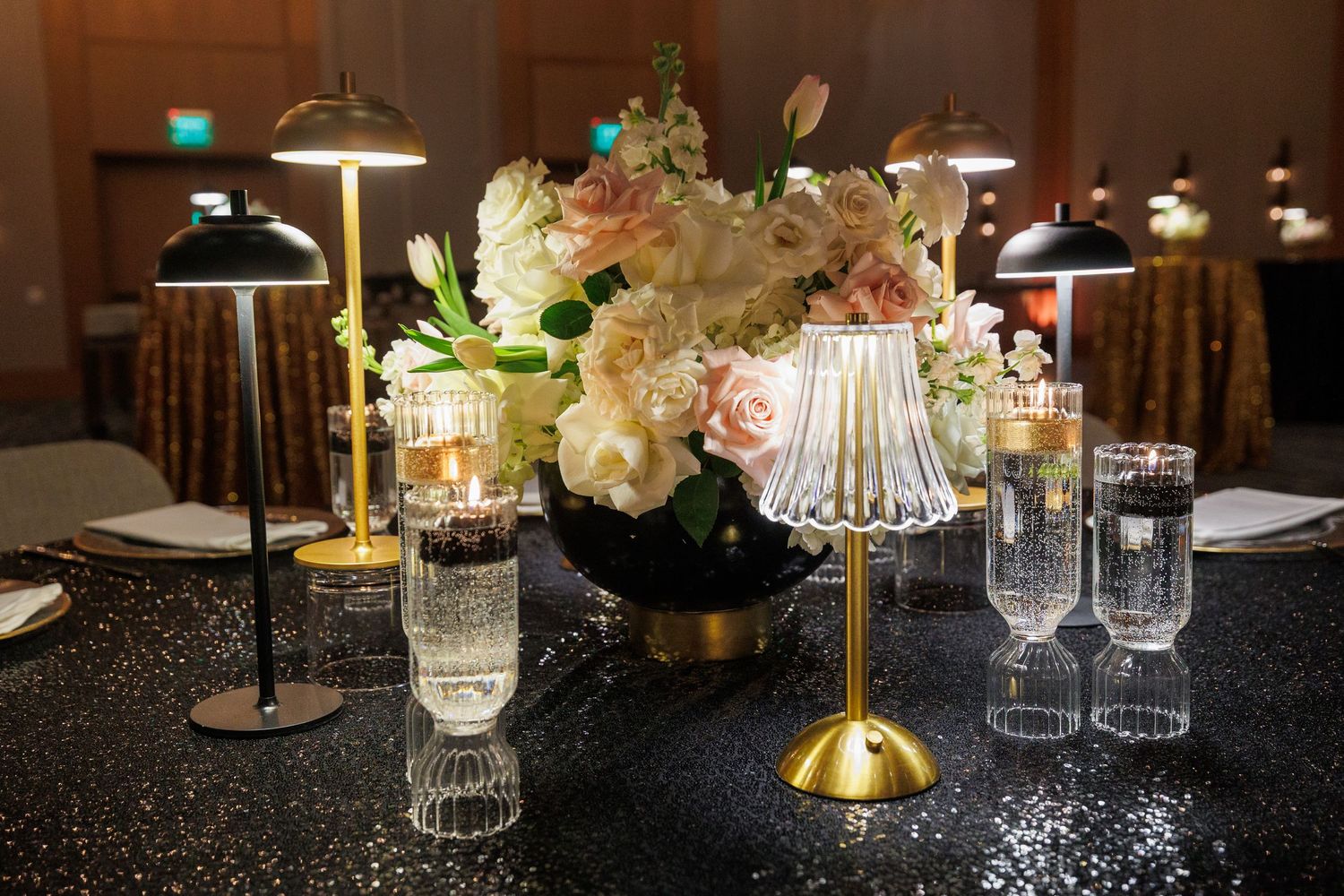 Elegant wedding reception table settings with crystal candle holders and floral centerpieces on dark sparkly tablecloths.