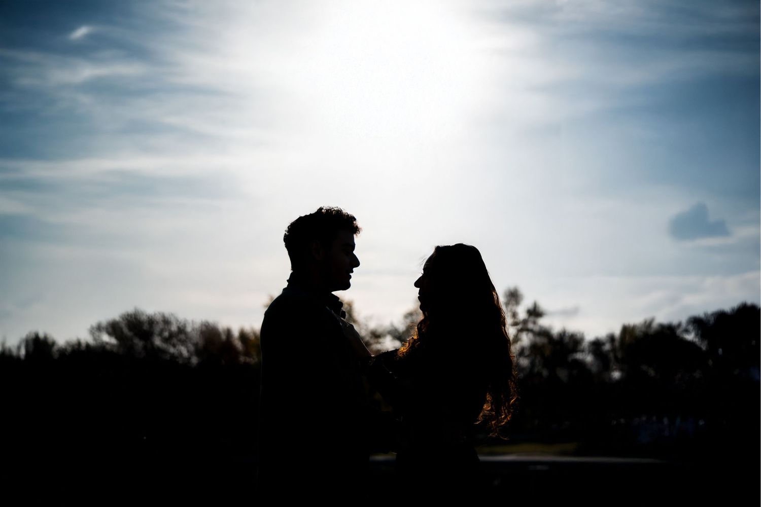Romantic silhouette of a couple standing together against a bright sky at sunset.