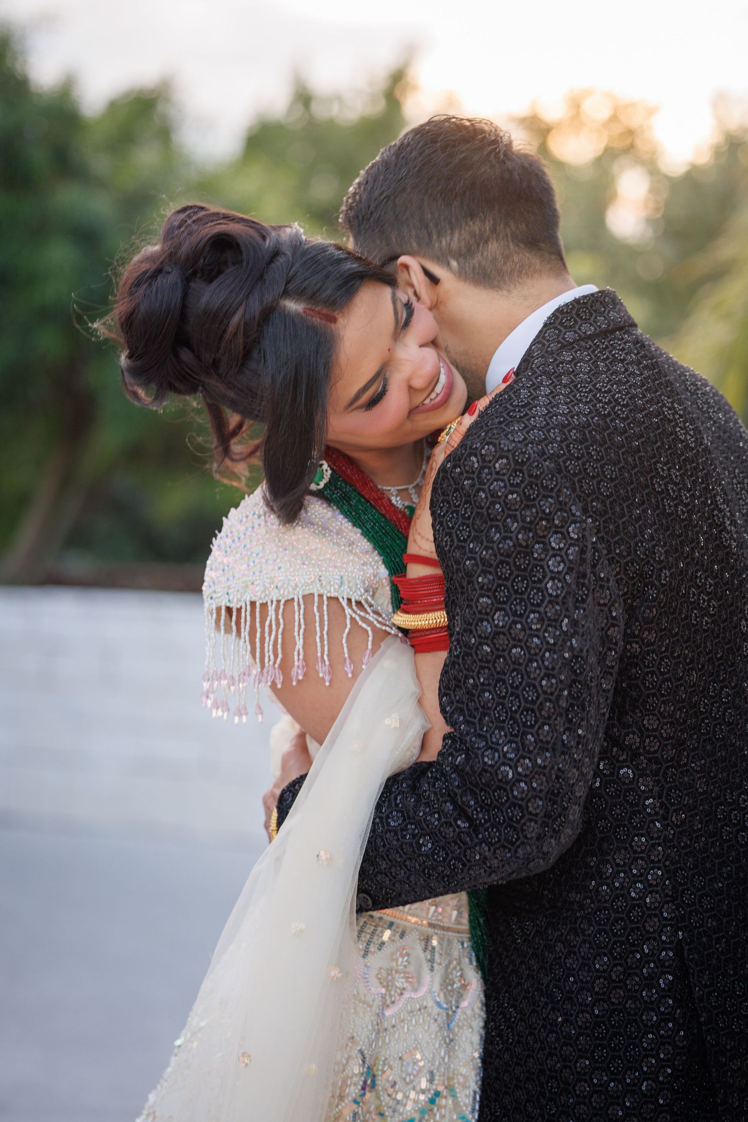 A couple in traditional wedding attire share a romantic embrace outdoors at golden hour.