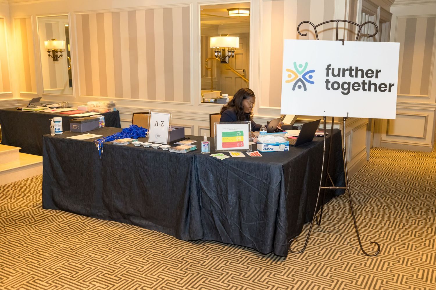 A panoramic view of an empty hotel conference room with tables set up along the walls and beige carpeting.