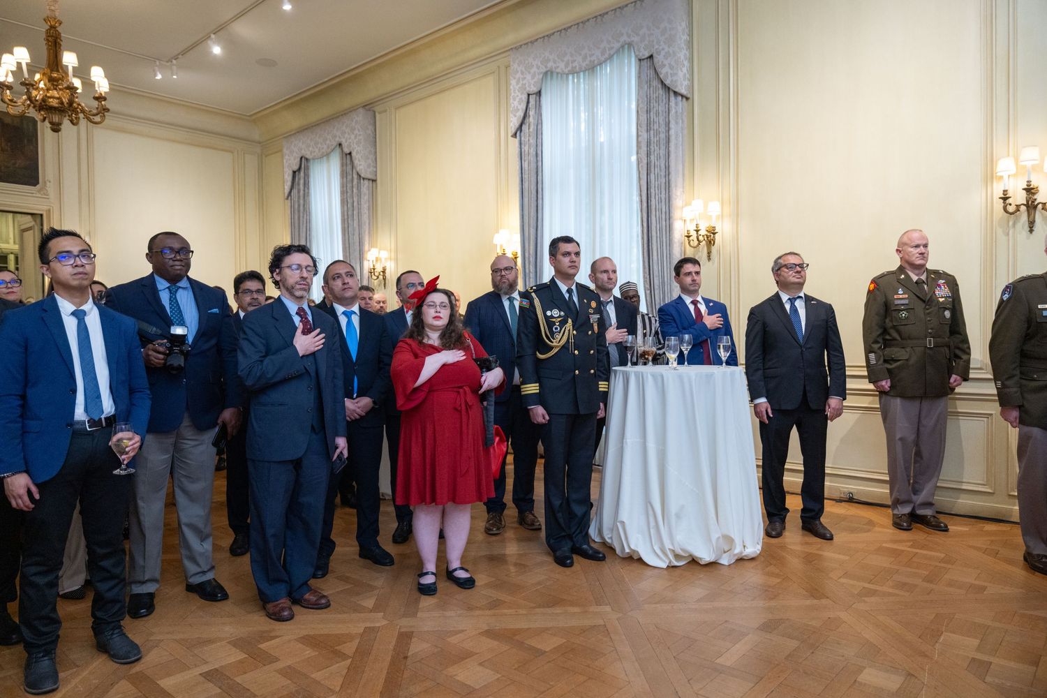 A panoramic view of people standing in a formal reception hall with elegant chandeliers and white walls.