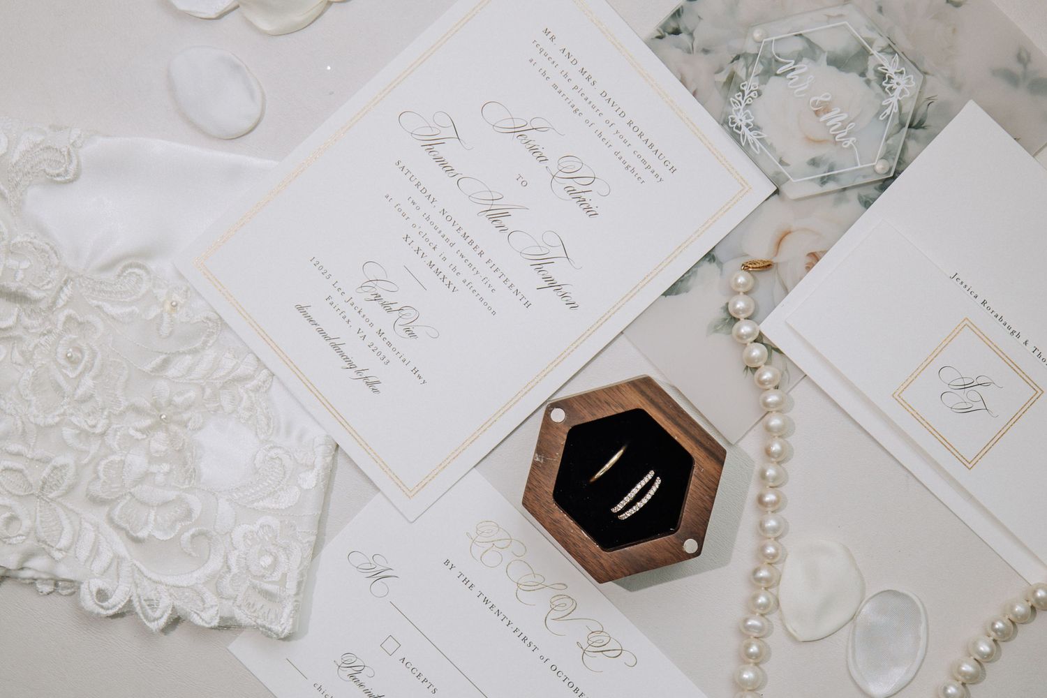 Luxury wedding stationery flatlay with gold-trimmed invitations, pearl necklace, and velvet ring box.