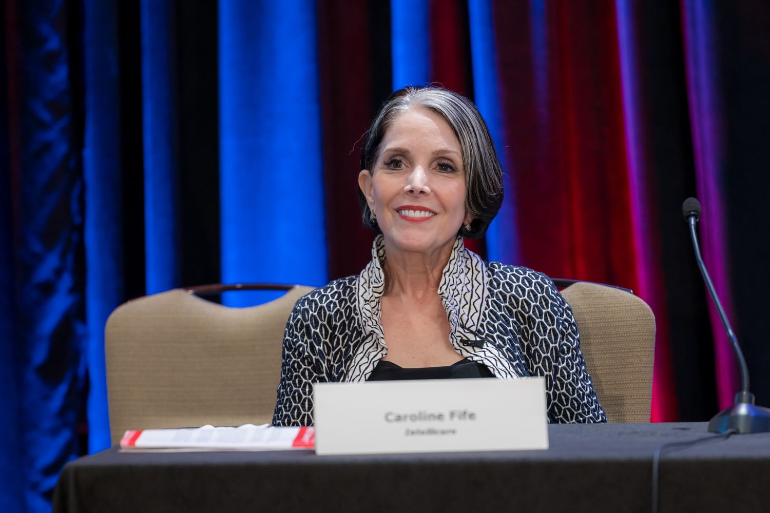Professional speaker panel discussion on stage with blue and red lighting at a conference event.