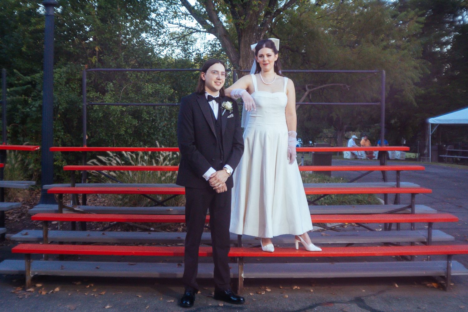 Wedding party poses on red bleachers at outdoor venue during sunset celebration.