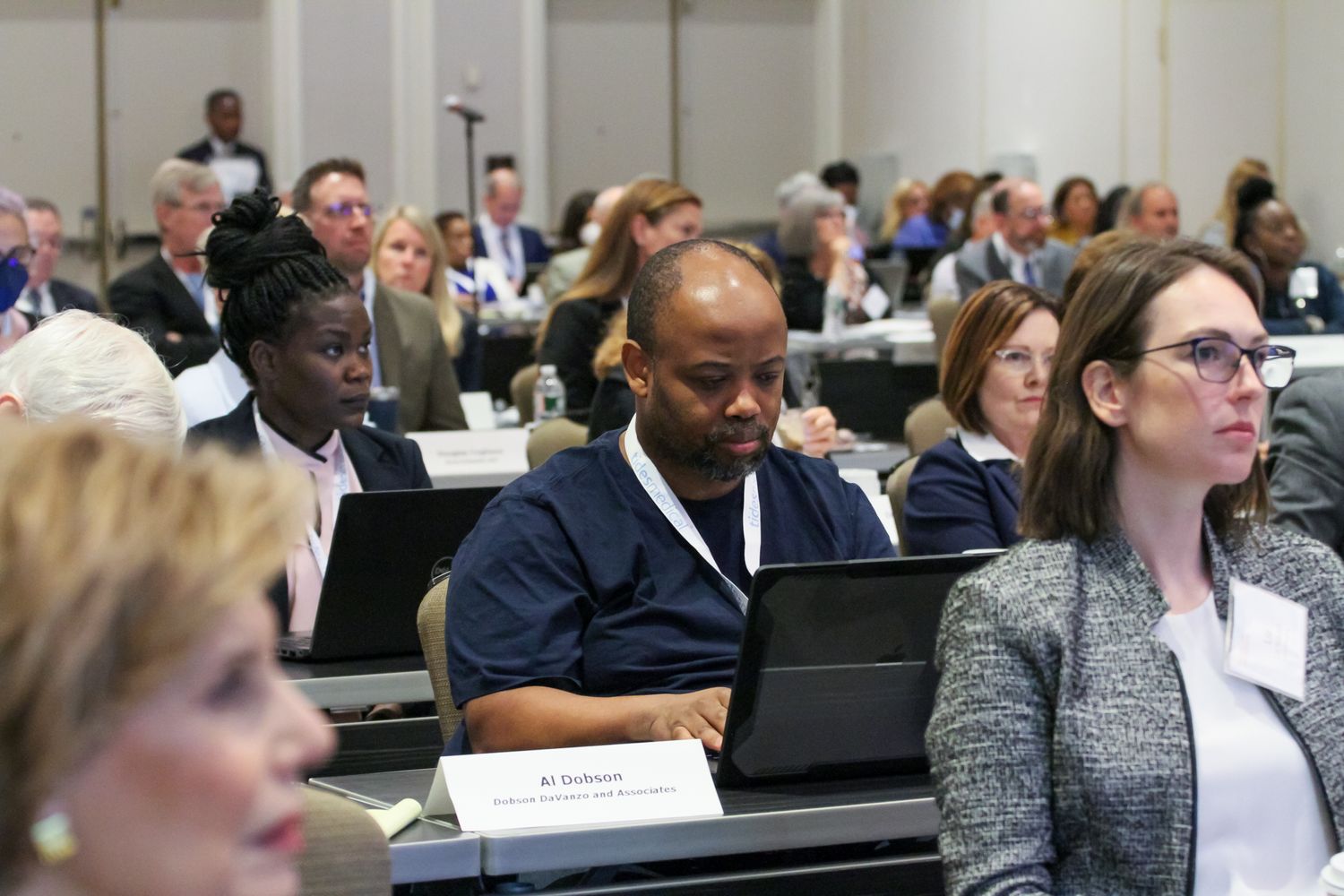 Diverse group of attendees listen intently during a corporate conference in a large meeting hall.