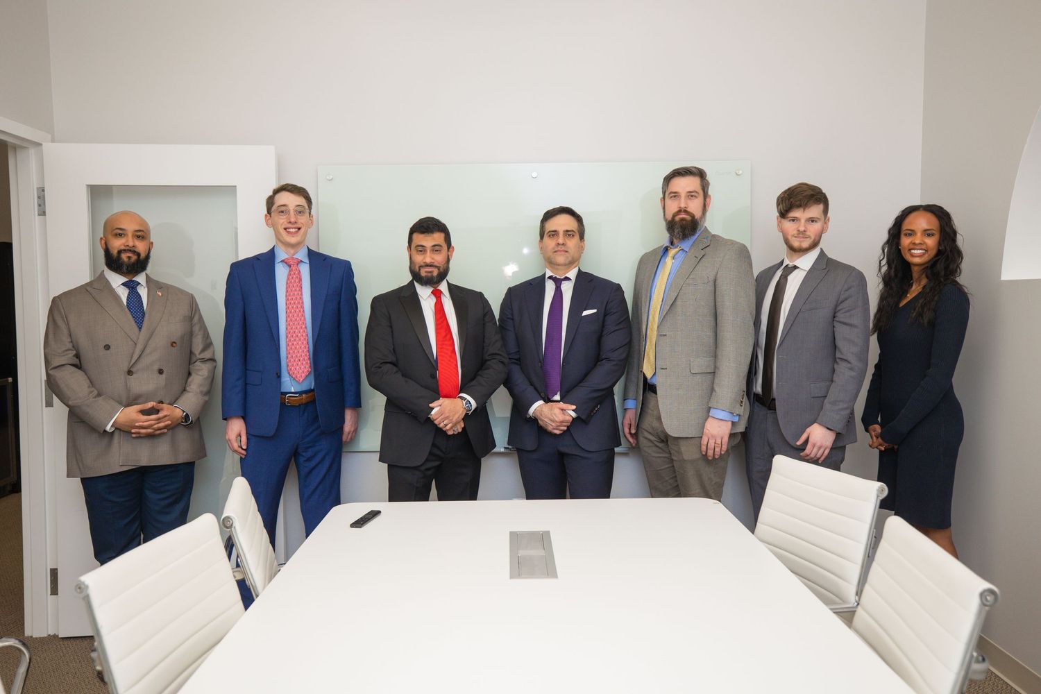 A group of professionally dressed people stand together in a business office setting.