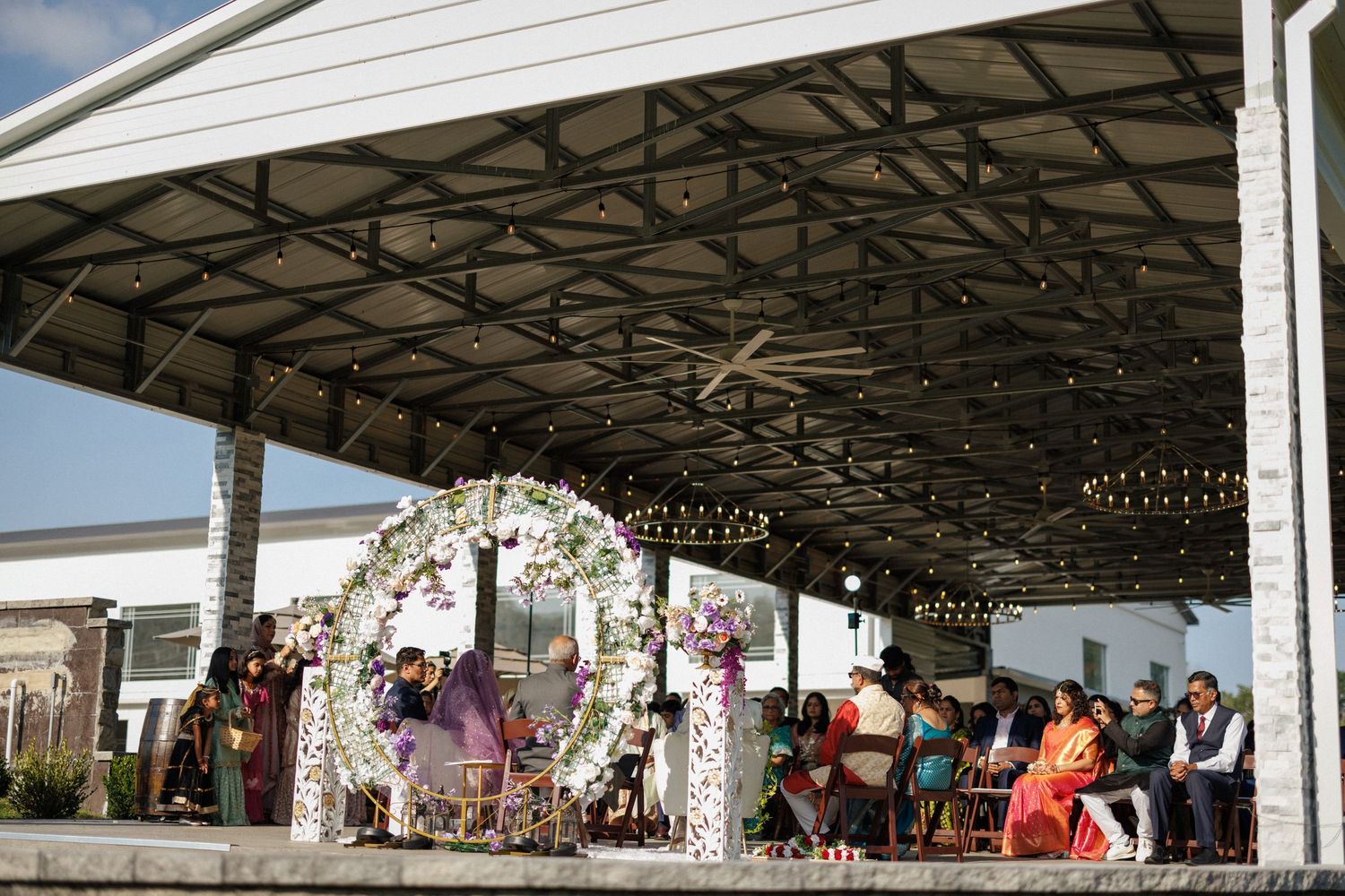 A panoramic view of an outdoor covered pavilion with white roof and support beams filled with event attendees.