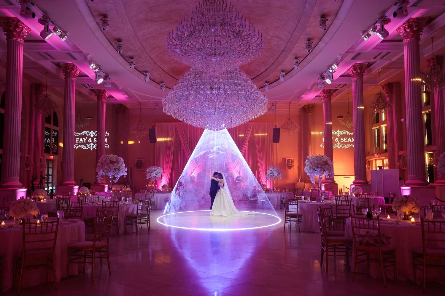 Elegant ballroom decorated with crystal chandeliers and purple uplighting creates a luxurious wedding reception atmosphere.