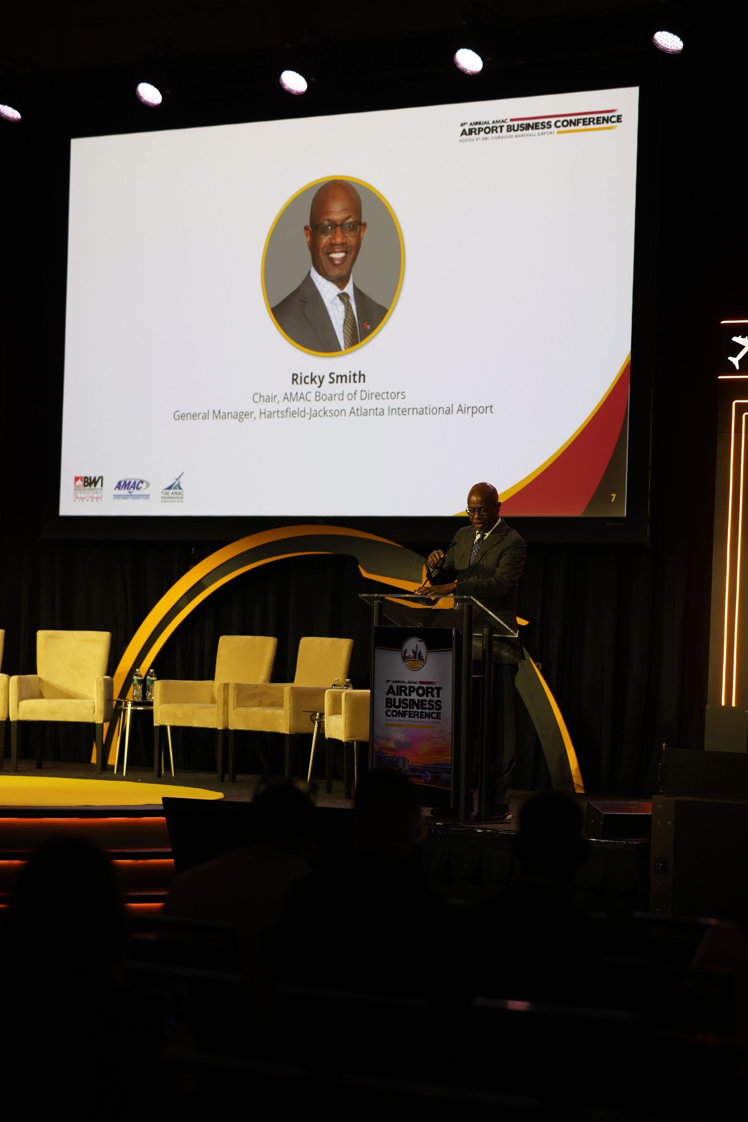 Ricky Smith, Chair of AMAC Board of Directors, speaks at podium during Airport Business Conference on stage.