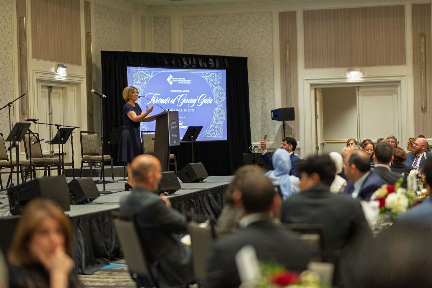 Business conference attendees seated in rows listen to a presentation in an elegant meeting room with white walls.