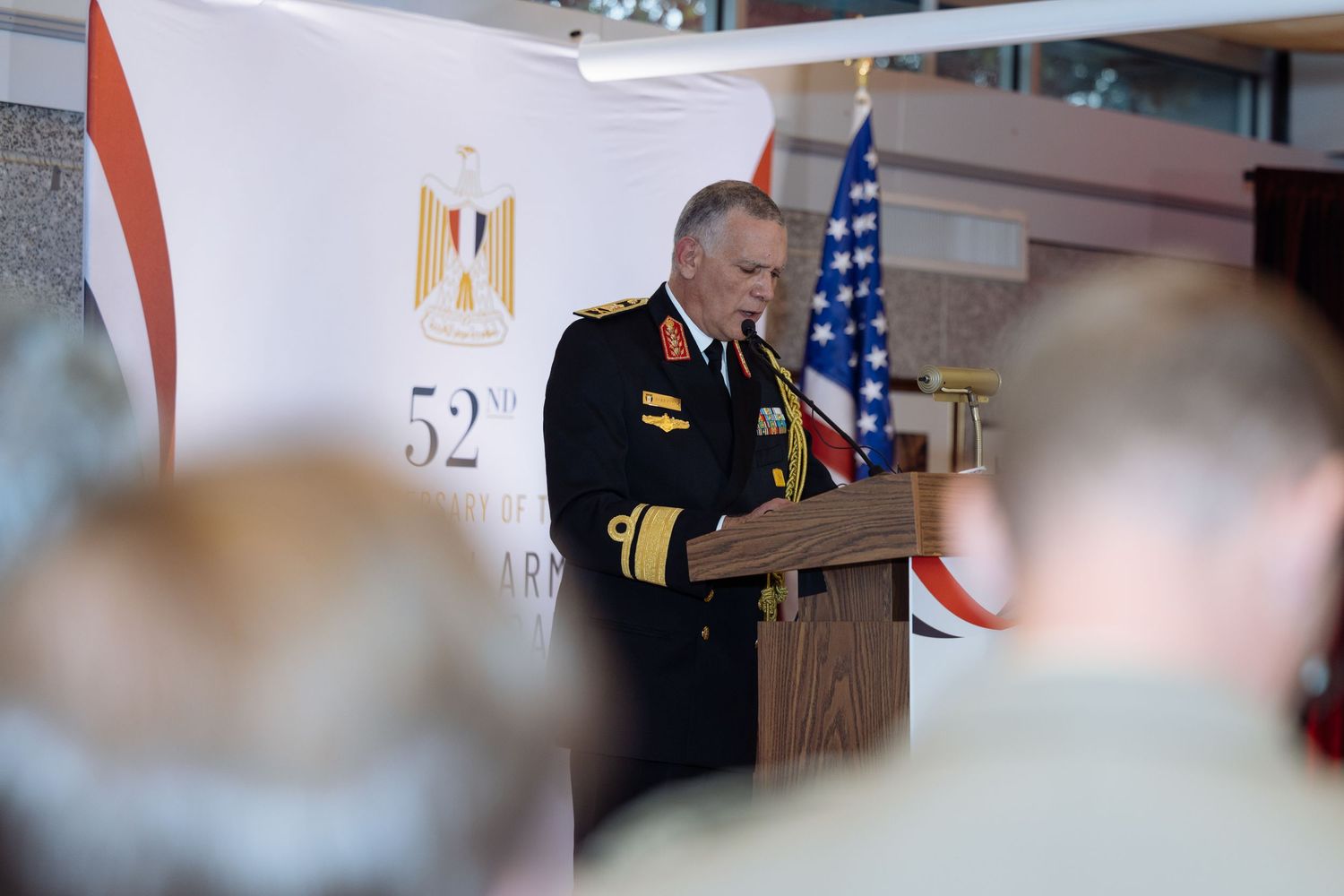 Military officials and dignitaries stand at podiums during a formal ceremony with American and Egyptian flags displayed.