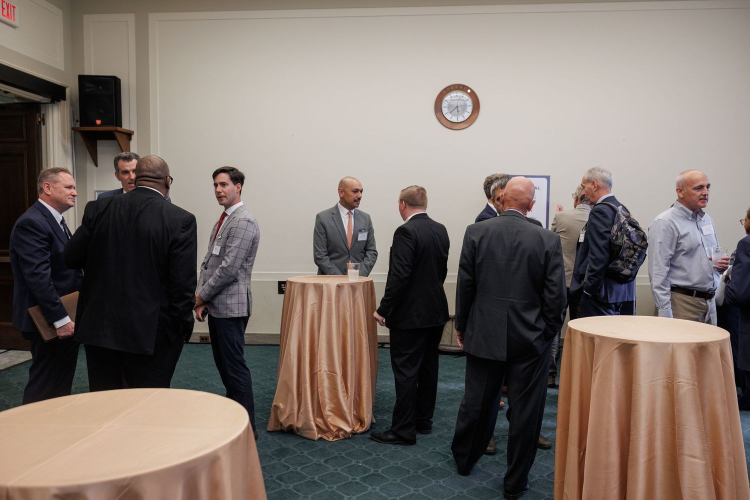 Business professionals networking at a formal cocktail reception in a banquet hall with round tables.