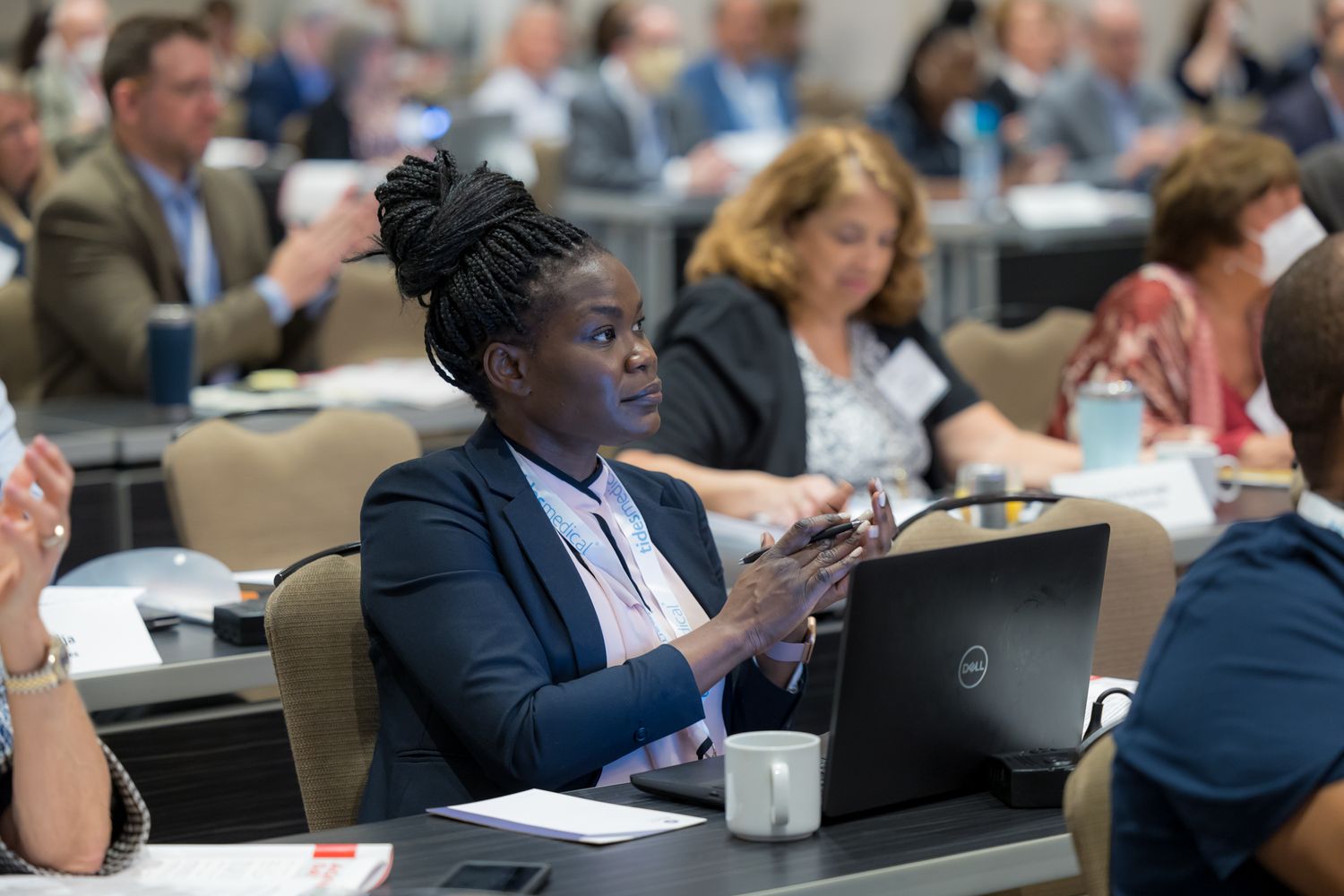 Business professionals sit in rows at a conference or meeting taking notes and listening to presentations.