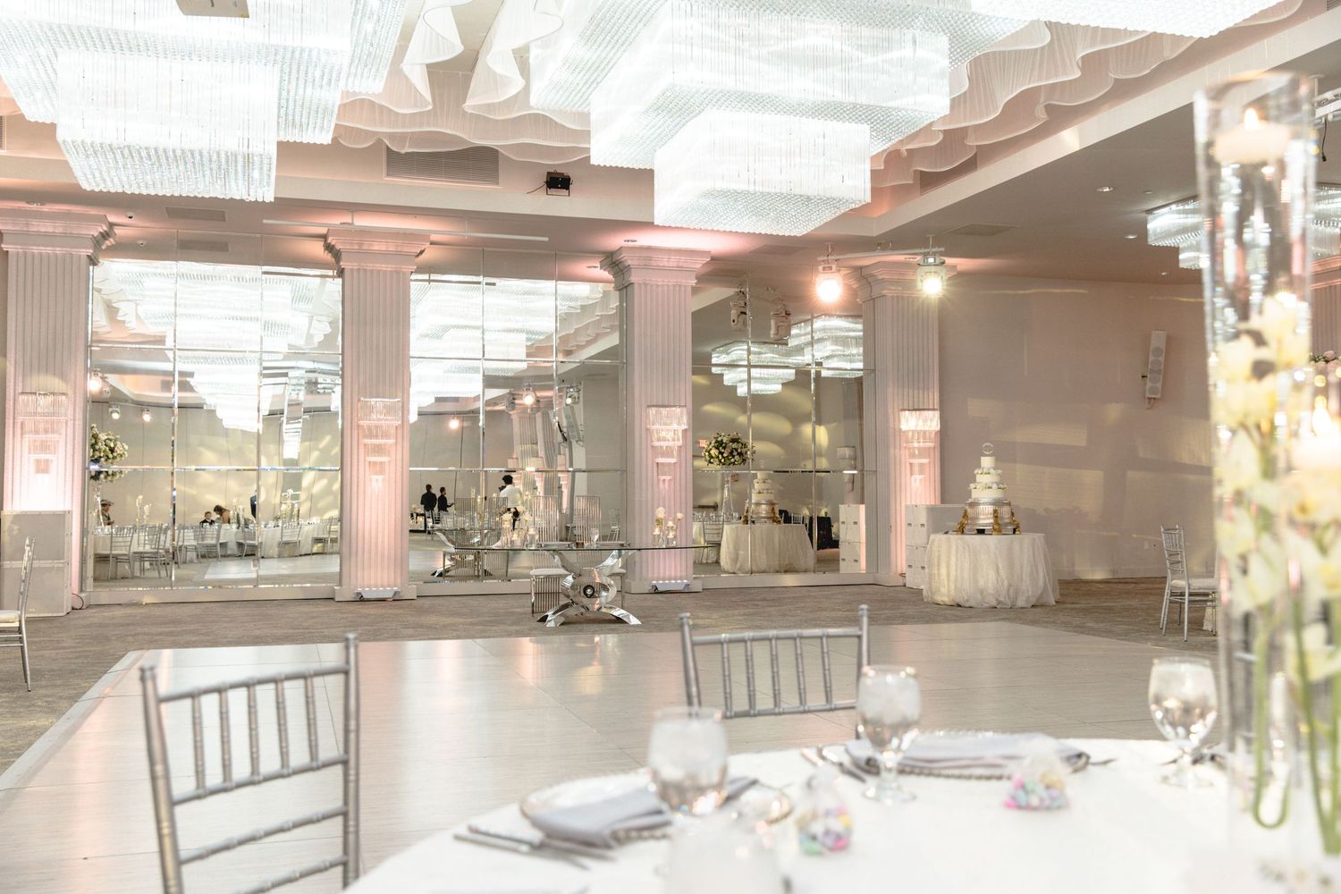Elegant wedding reception venue with pink columns, mirrored walls, and formal table settings in soft lighting.
