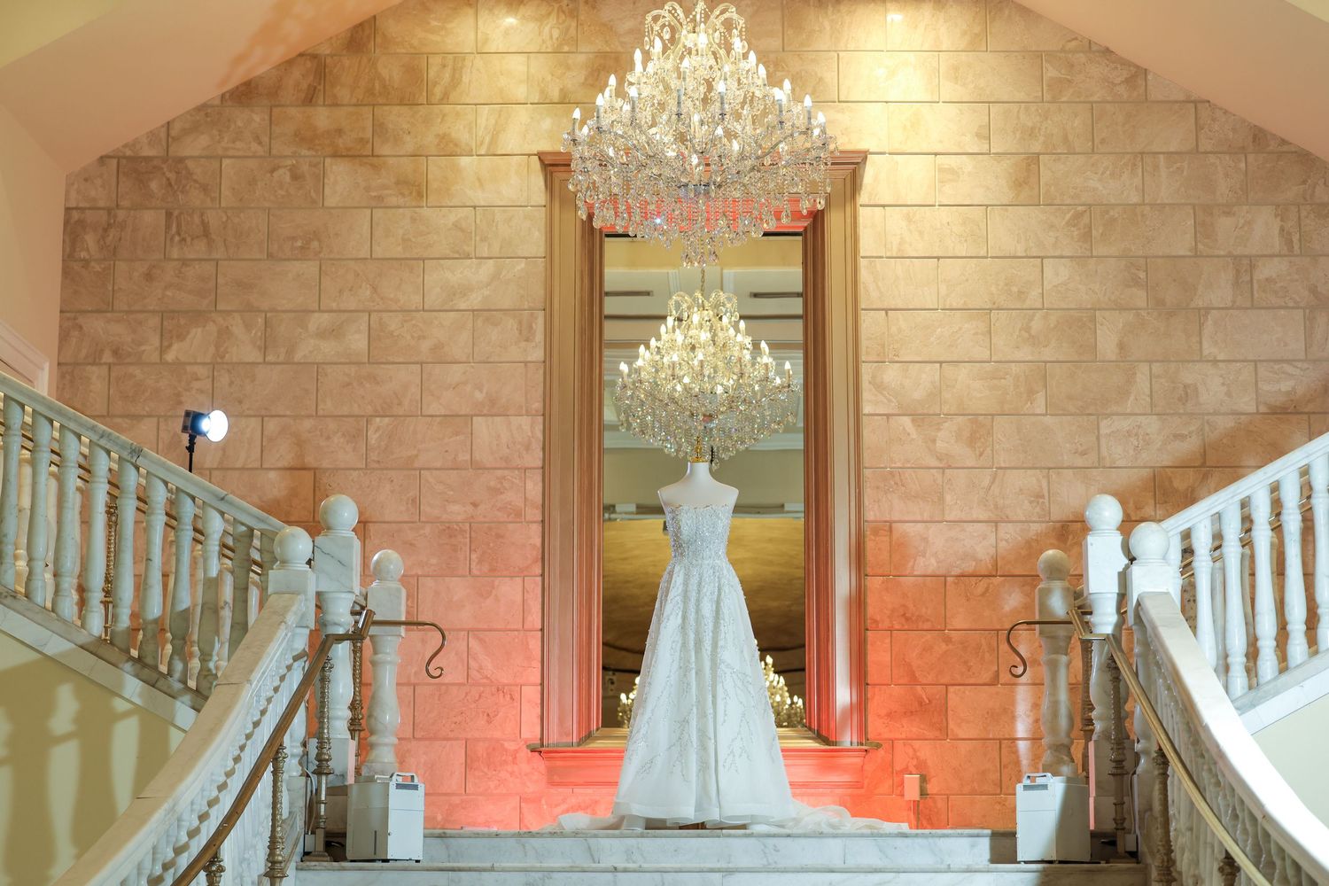 Elegant wedding venue panorama showing brick walls, crystal chandeliers, and white decor in warm lighting.