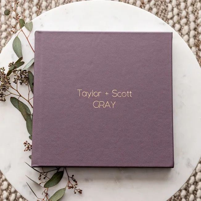 Purple wedding photo album cover with gold text on white plate with greenery.