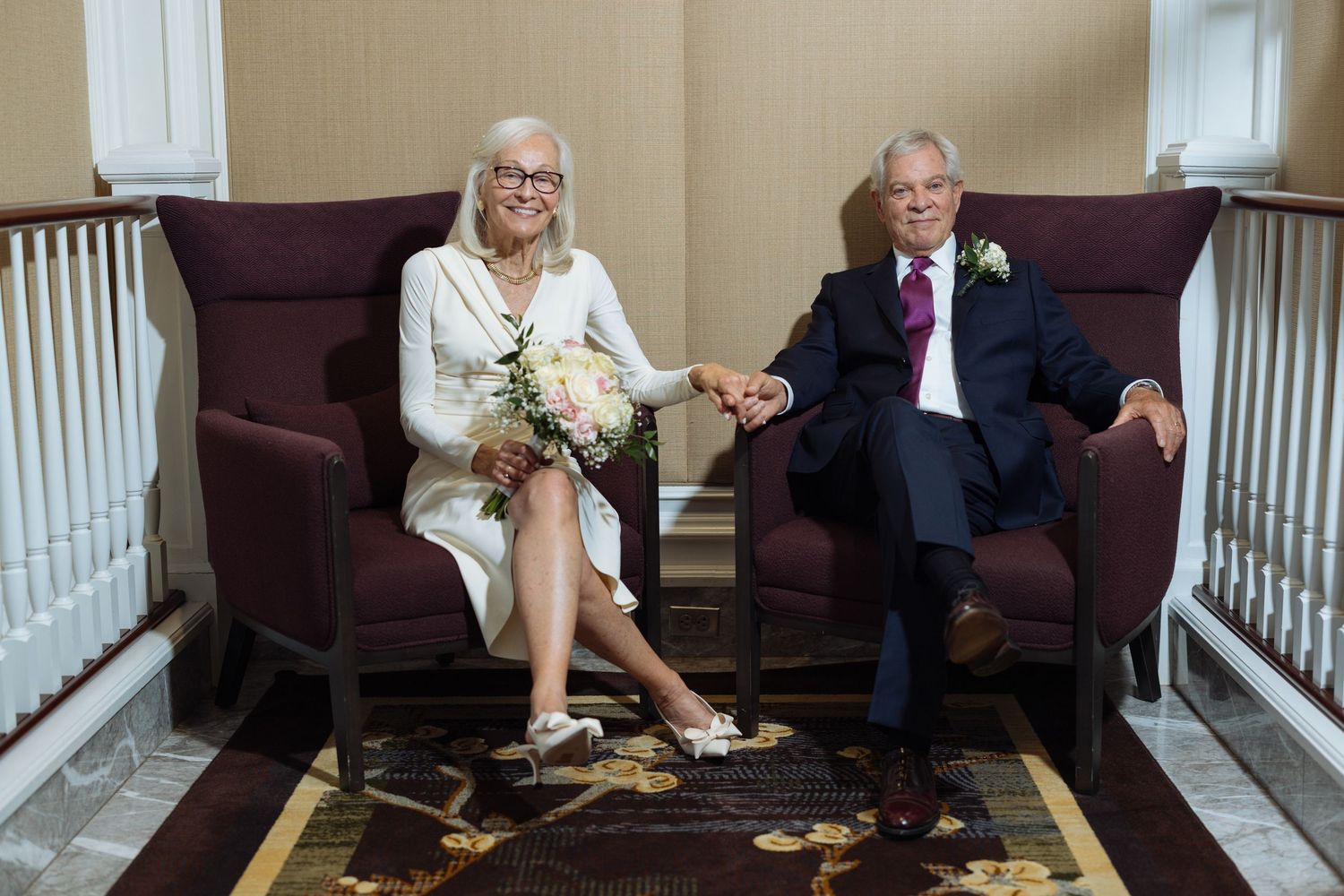 People sitting on stairs and floor in a casual indoor setting with white railing and dark carpeting.