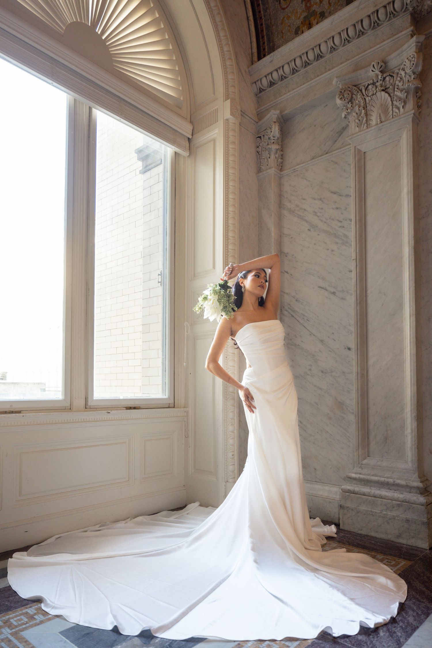 A flowing white wedding dress with a dramatic train is photographed in sequence against ornate marble walls and windows.