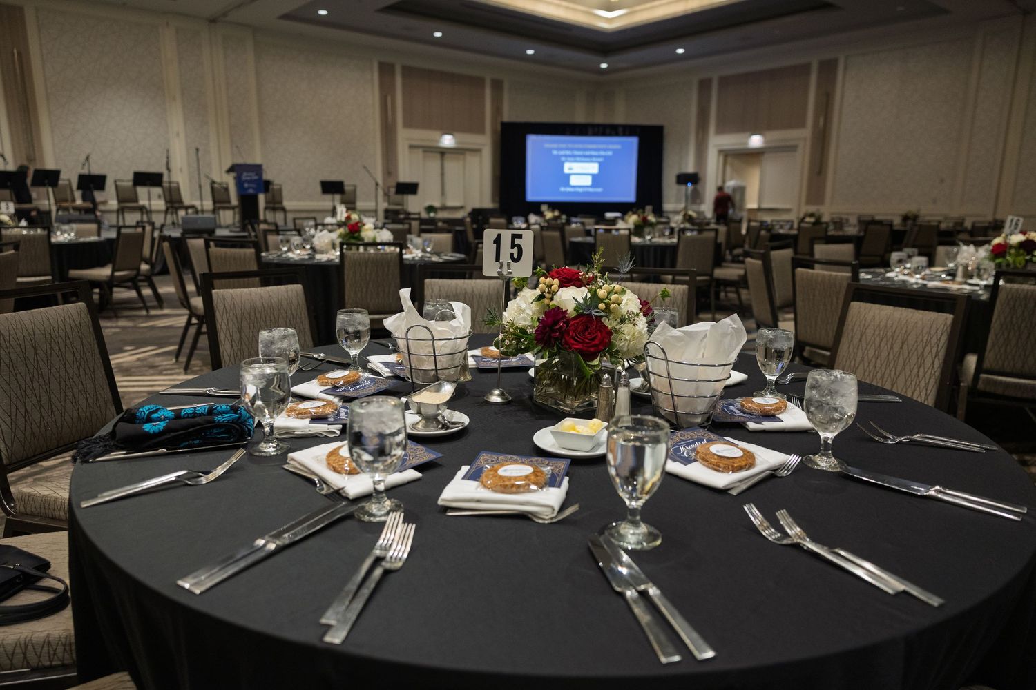 A banquet hall with multiple round tables set for a formal event, featuring elegant place settings and ambient lighting.