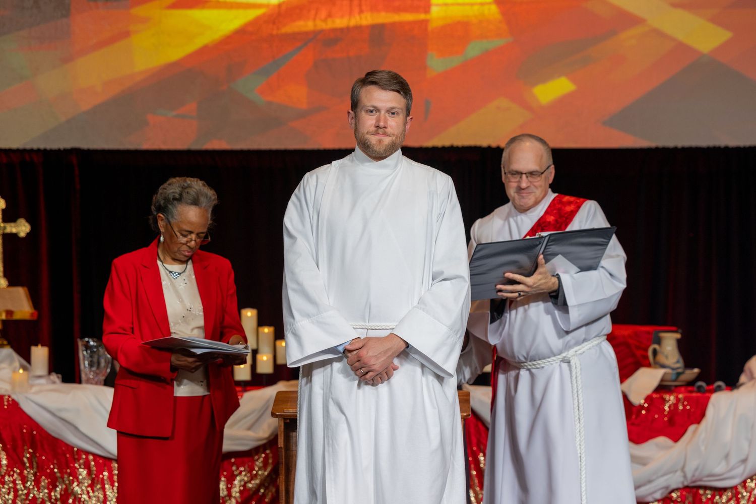 A group of clergy members in red and white robes stand together during a religious ceremony.