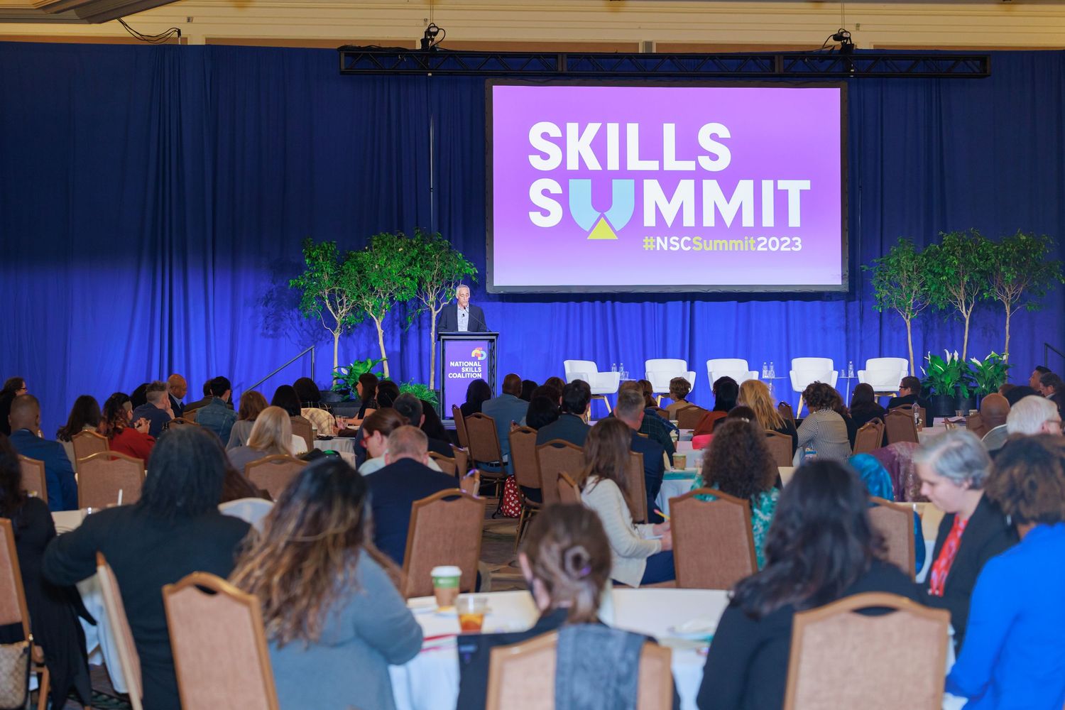 Business conference audience sitting in rows of chairs watching presentation at professional skills summit event.